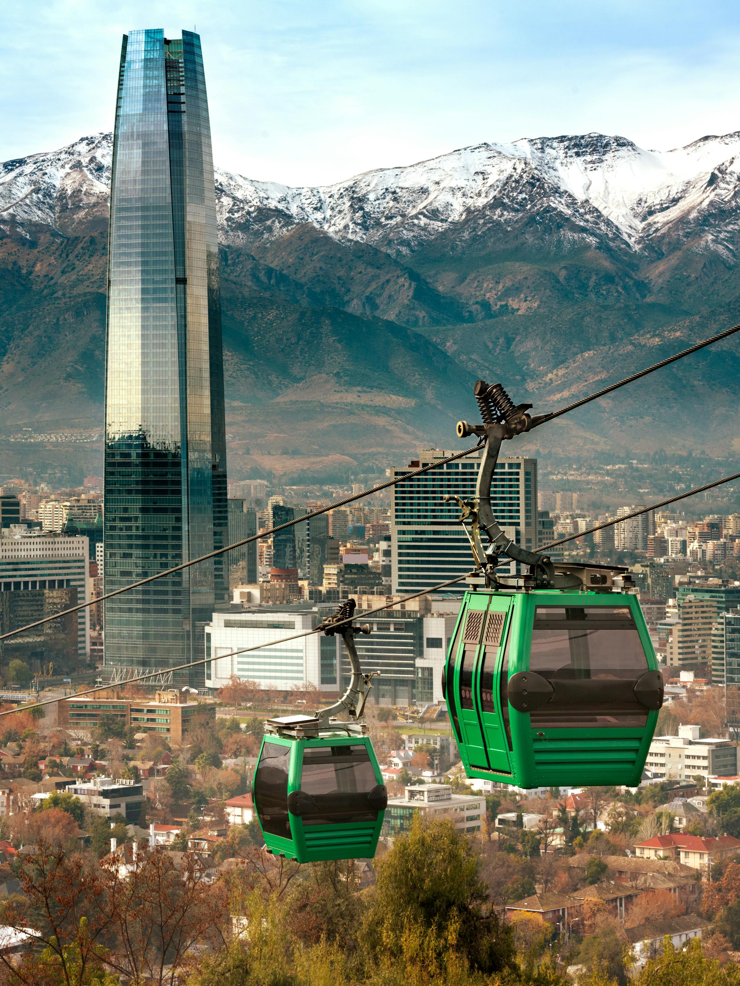 Green cable cars glide above Santiago toward the Andes, with high-rises below and snowy peaks behind them.