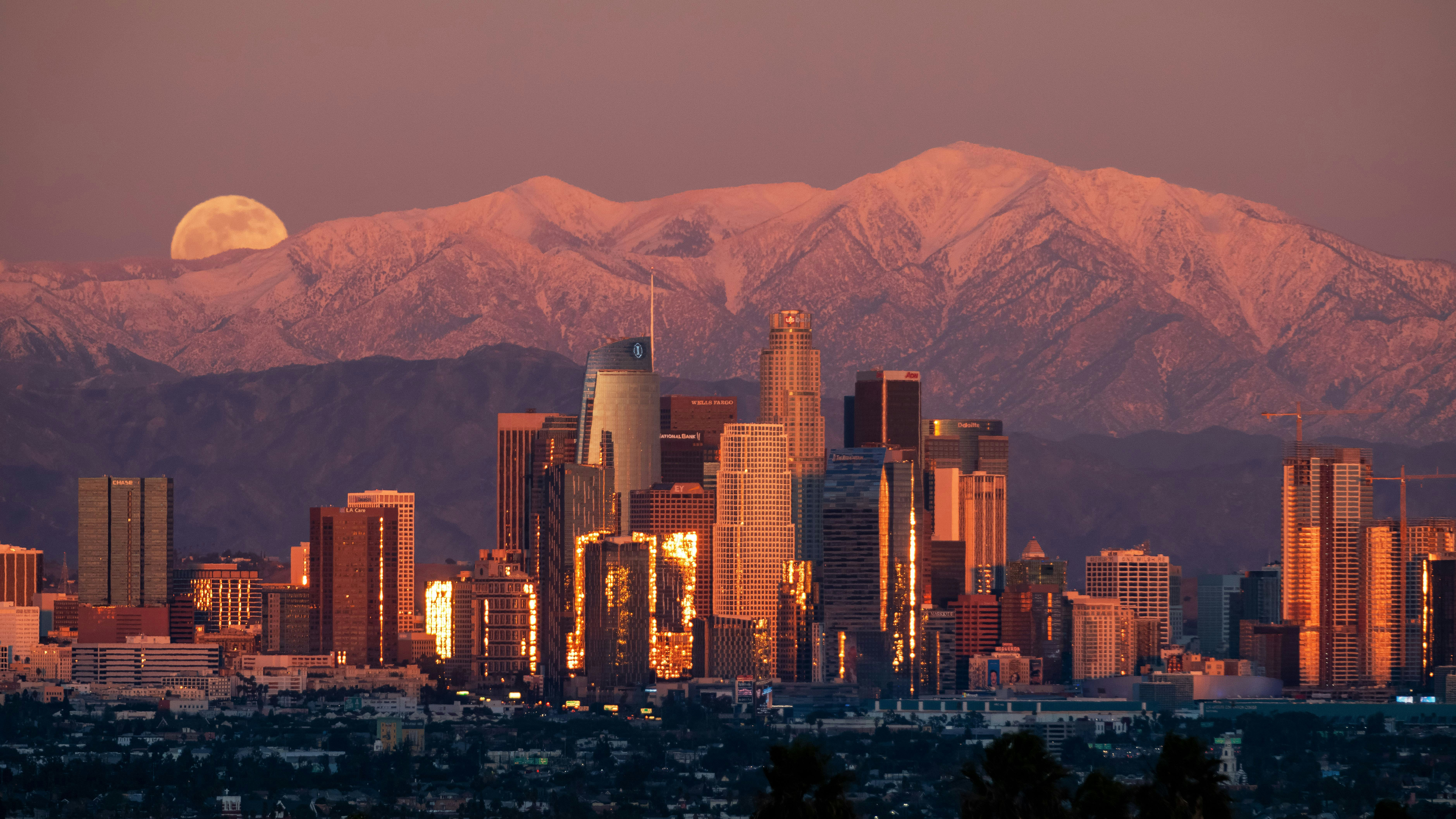 Santiago’s towers glow at dusk beneath a rising moon, with the Andes peaks tinted pink behind them softly.
