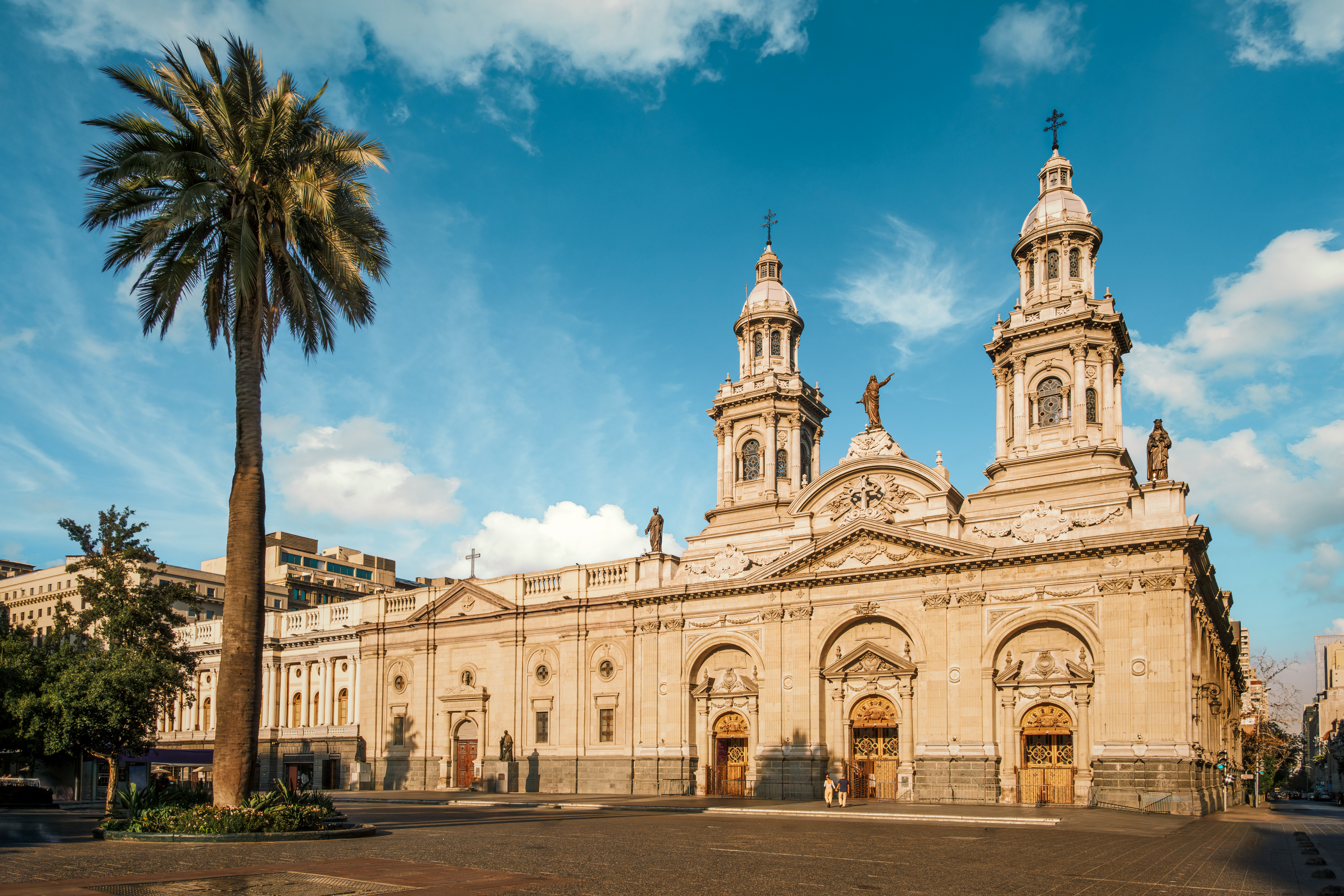 The Metropolitan Cathedral of Santiago stands in Plaza de Armas, with a palm framing its twin towers in sun.
