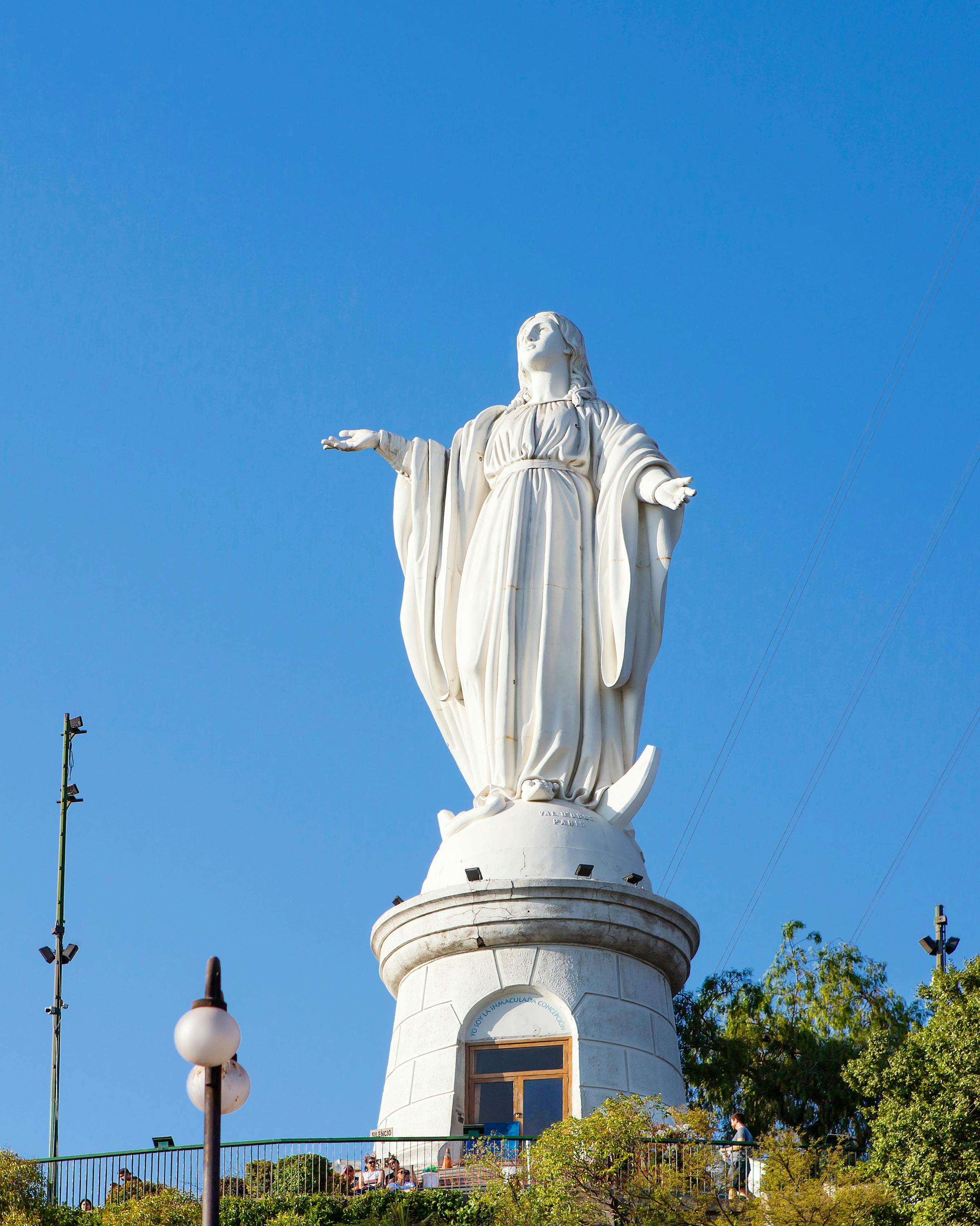 The white statue of the Virgin Mary rises above Cerro San Cristóbal, with palms under a clear blue sky above.