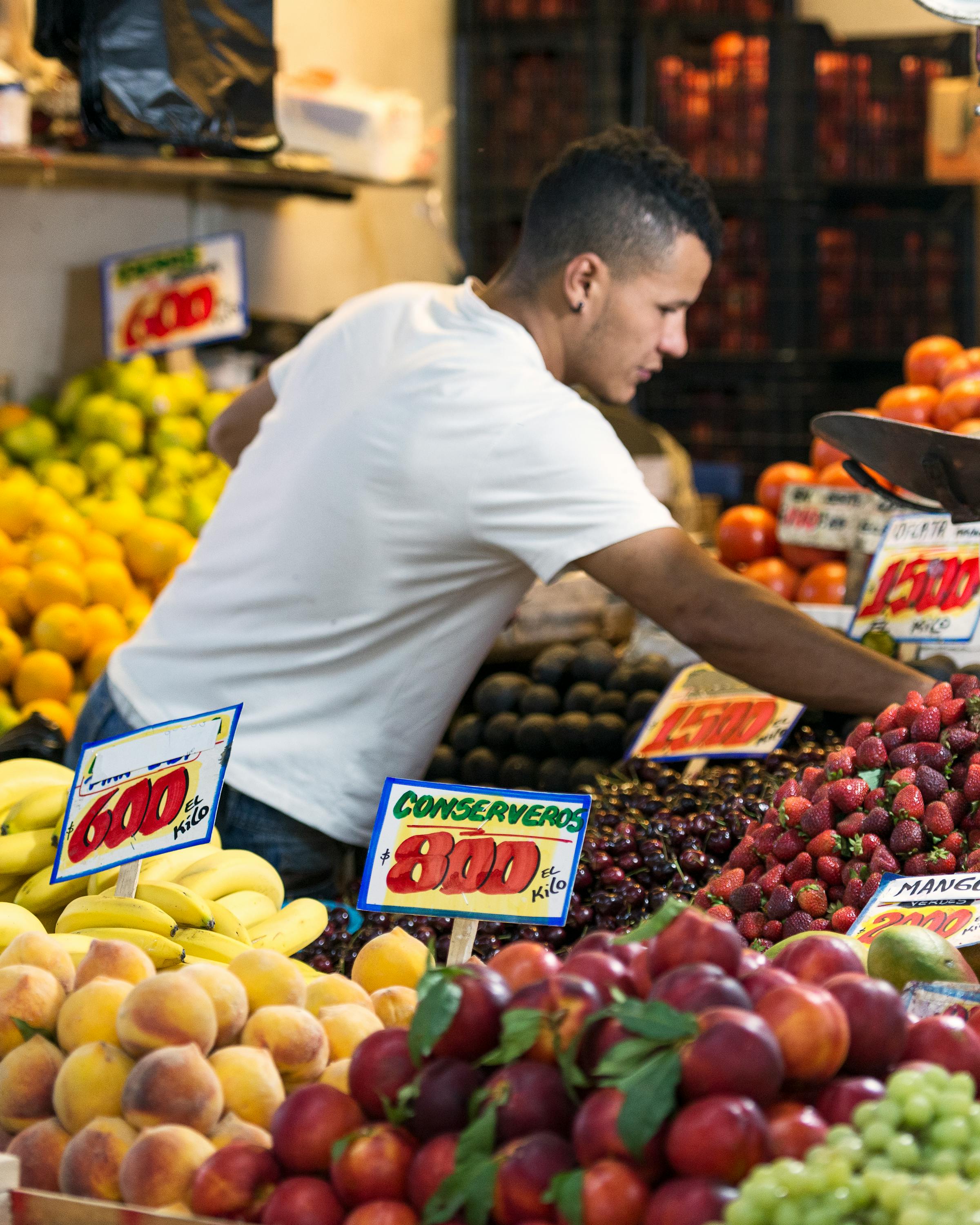 A vendor arranges fruit at a Santiago market stall, with oranges and berries stacked in colorful rows around him.