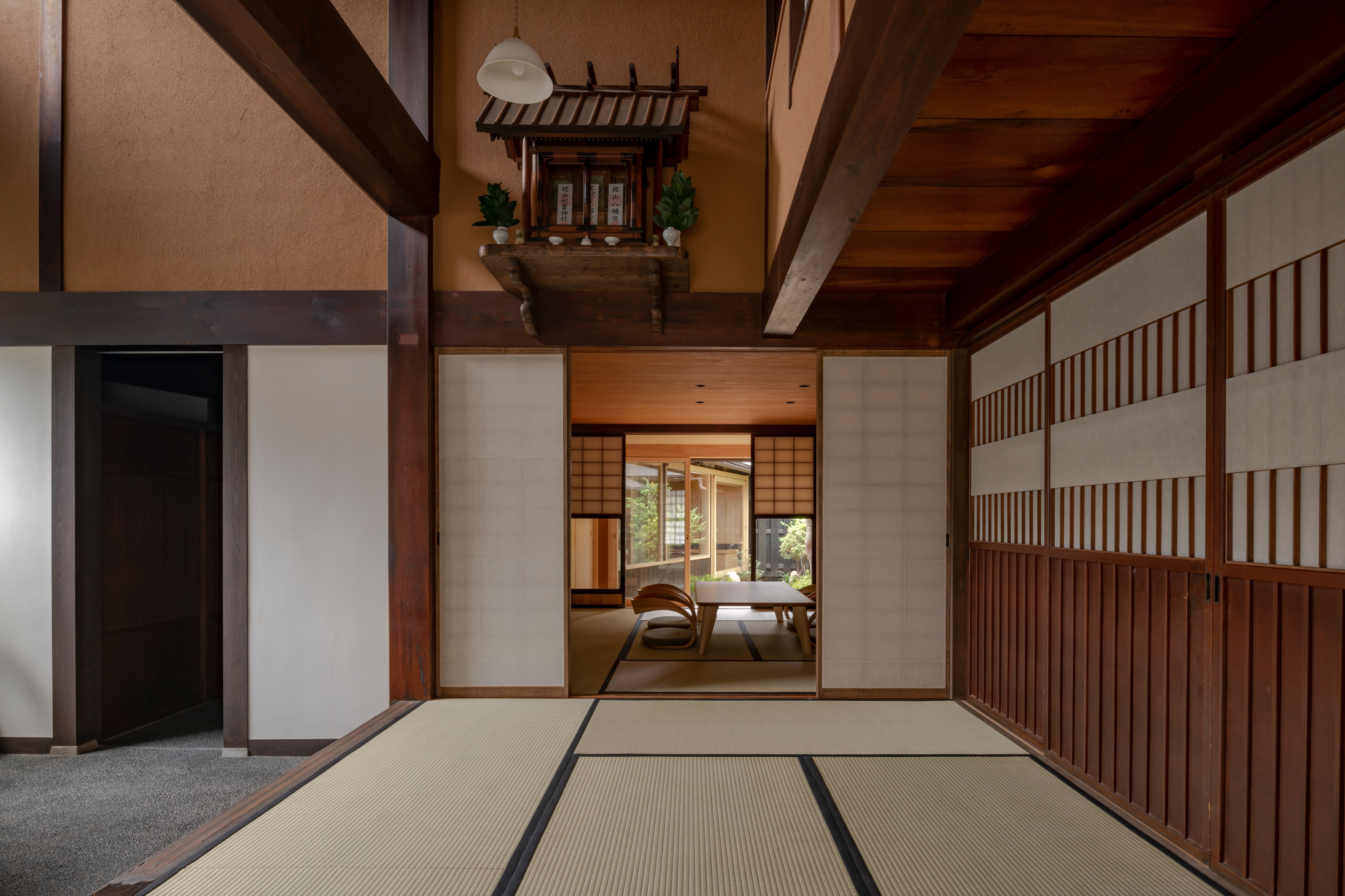 A quiet tatami room with sliding doors leads to a sitting area, with a kamidana shrine above the hallway.