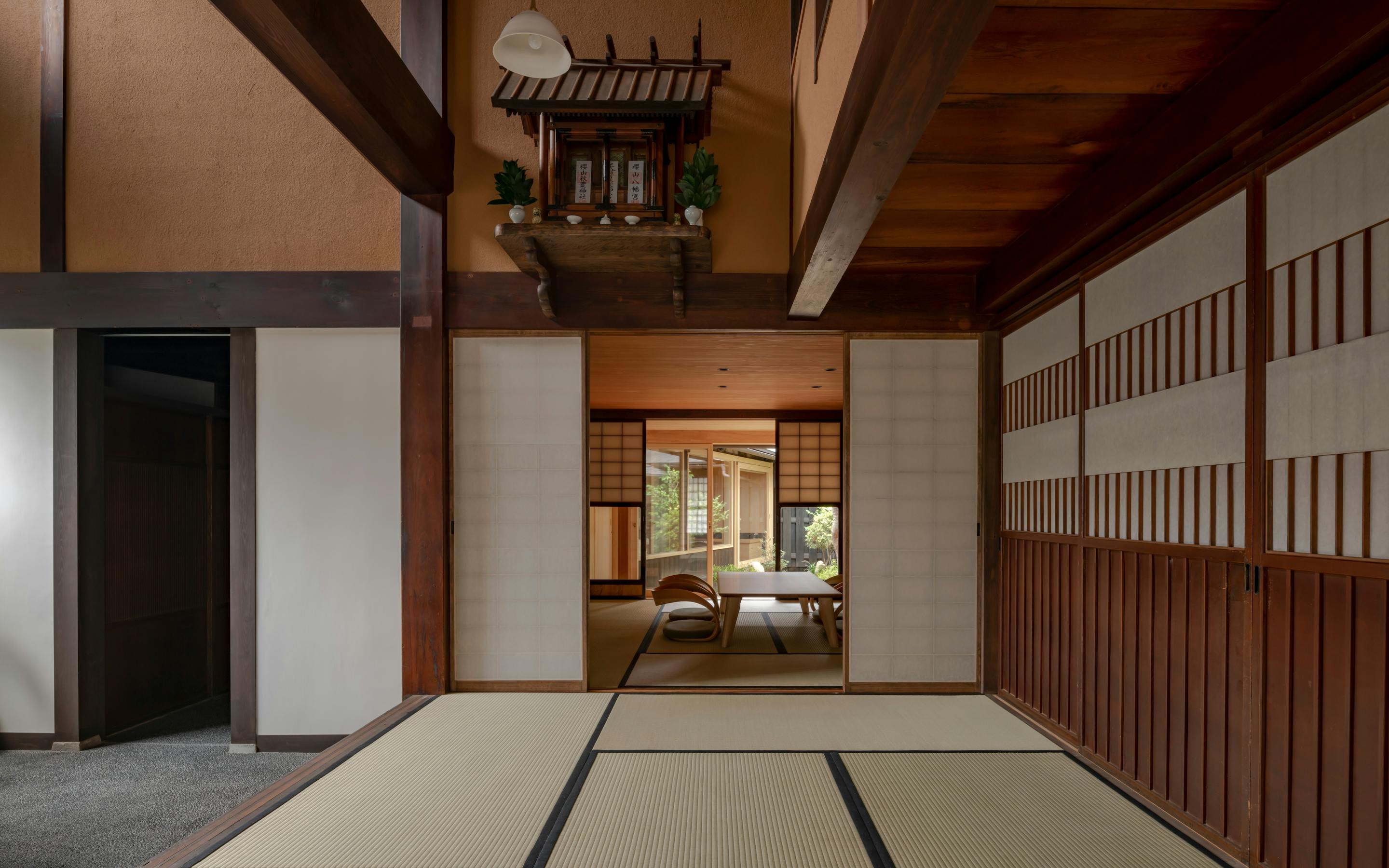 A quiet tatami room with sliding doors leads to a sitting area, with a kamidana shrine above the hallway.