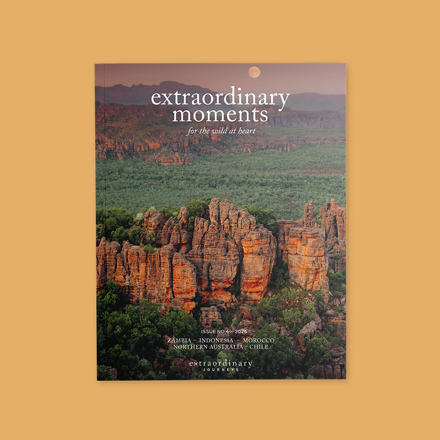 Cover of “Extraordinary Moments” magazine featuring a dramatic landscape of rugged orange rock formations rising above a lush green forest at sunset, with a full moon in the sky. Text reads: “extraordinary moments – for the wild at heart.” Issue No. 4, 2026.