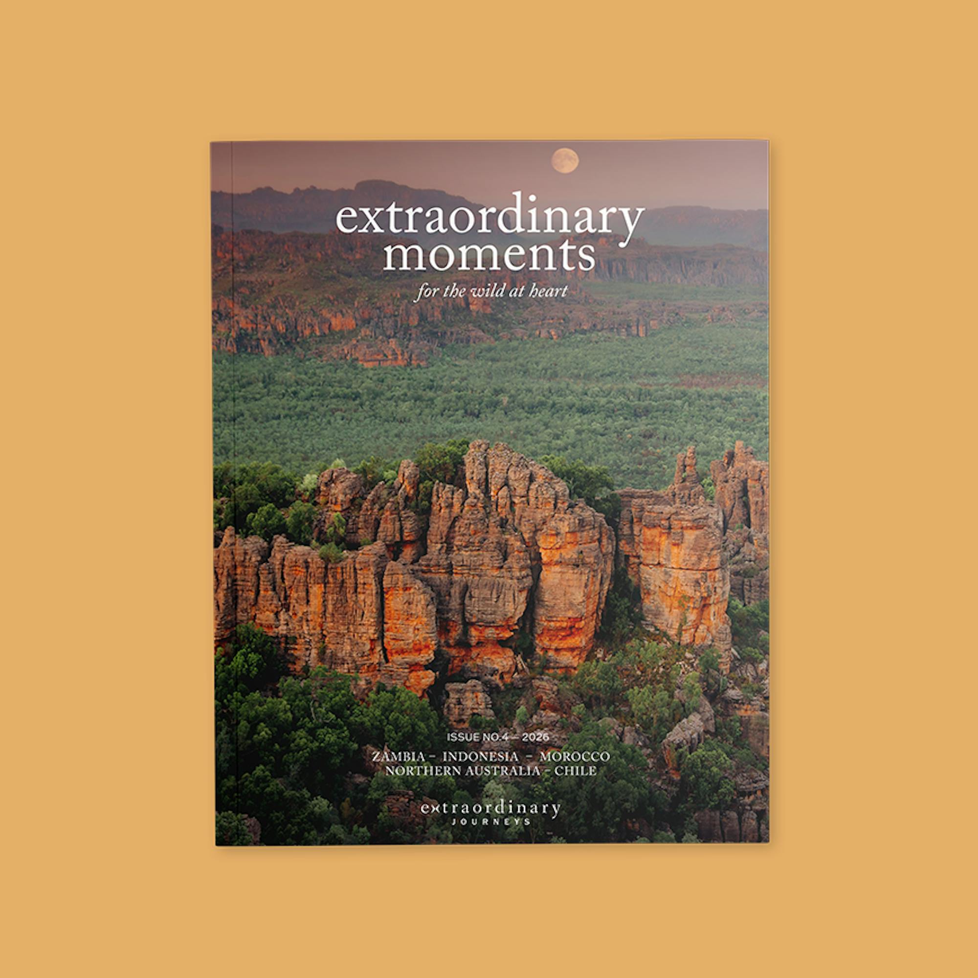 Cover of “Extraordinary Moments” magazine featuring a dramatic landscape of rugged orange rock formations rising above a lush green forest at sunset, with a full moon in the sky. Text reads: “extraordinary moments – for the wild at heart.” Issue No. 4, 2026.