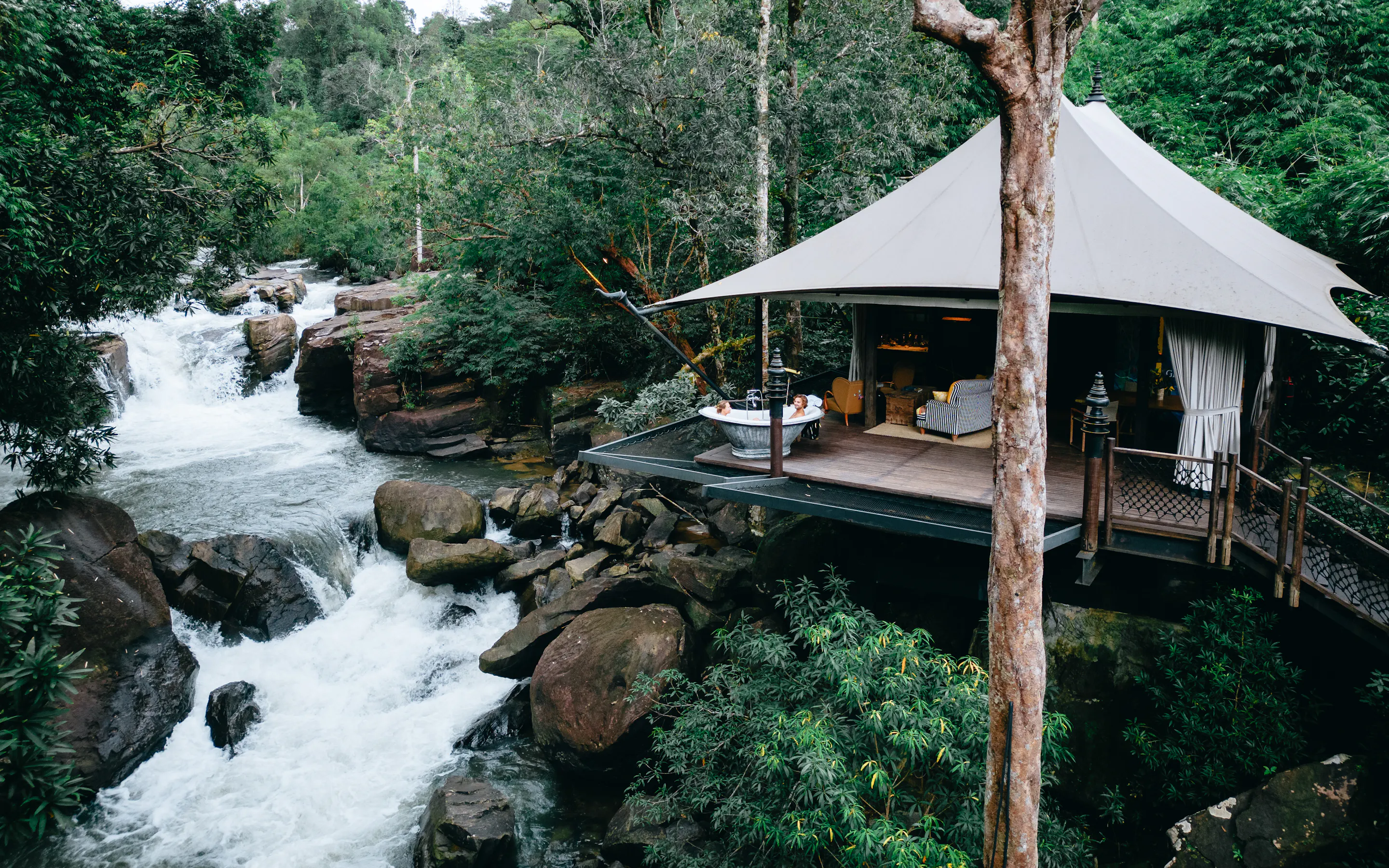 tent next to river rapids in green jungle