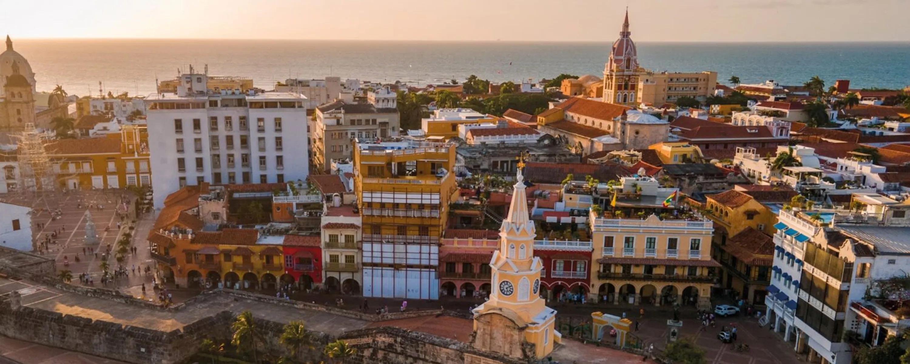Golden light washes over Cartagena's old city, where church towers and terracotta roofs rise beside the sea.