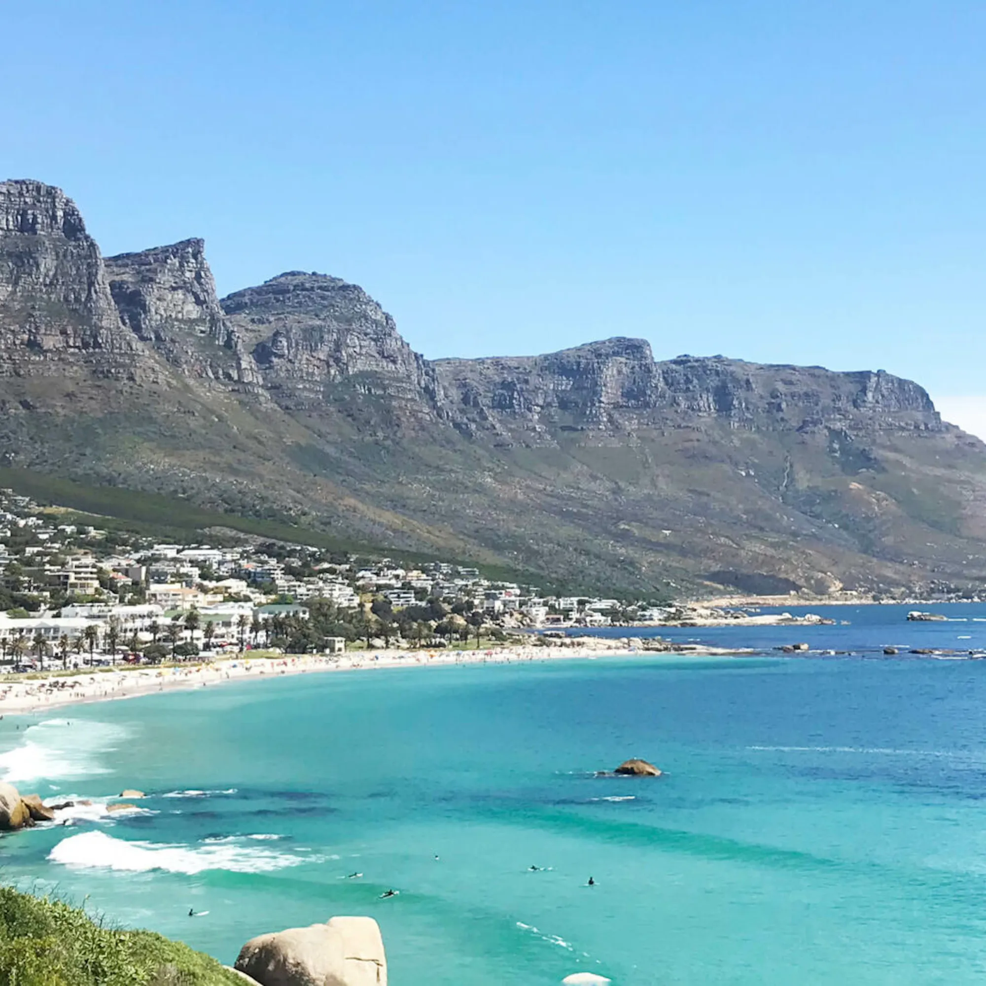 Camps Bay beach with the Twelve Apostles beyond against the backdrop of Cape Town beneath clear skies.