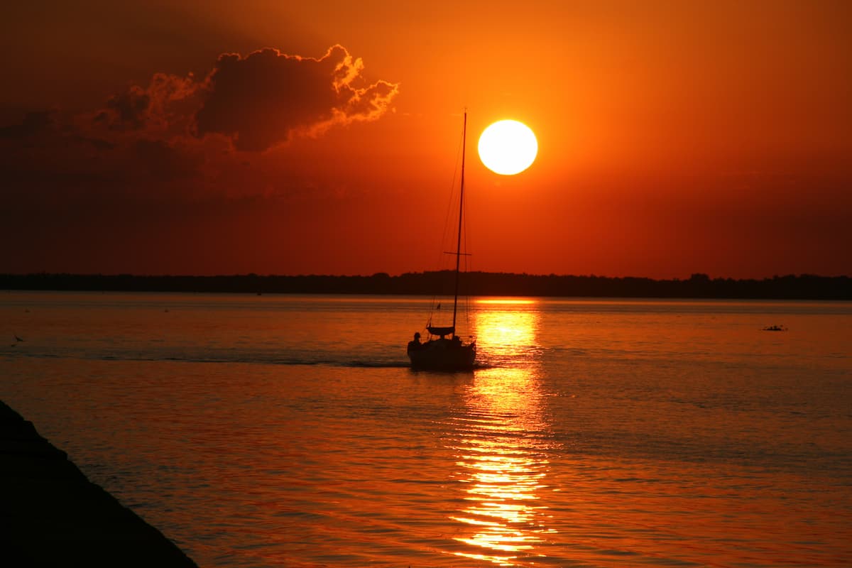 A small boat glides across the glowing Rio de la Plata at sunset, framed by deep orange water and sky in Carmelo.