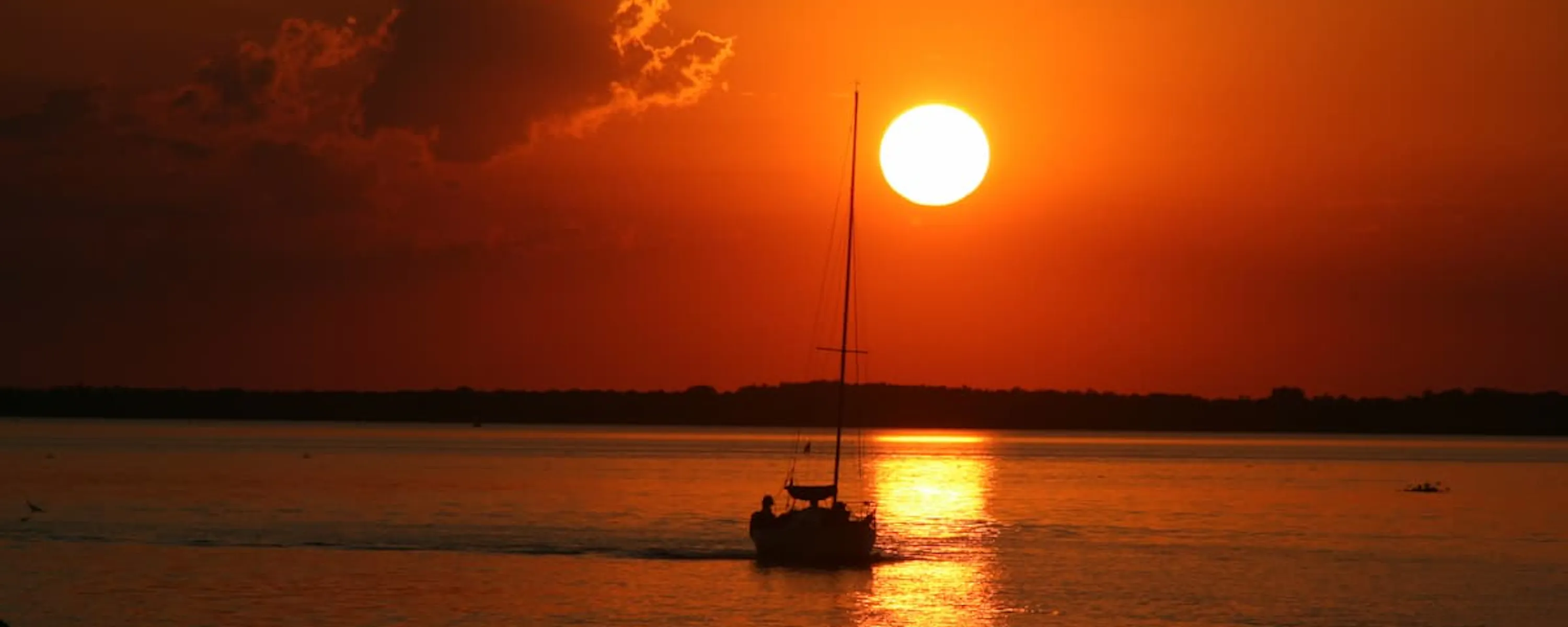 A small boat glides across the glowing Rio de la Plata at sunset, framed by deep orange water and sky in Carmelo.