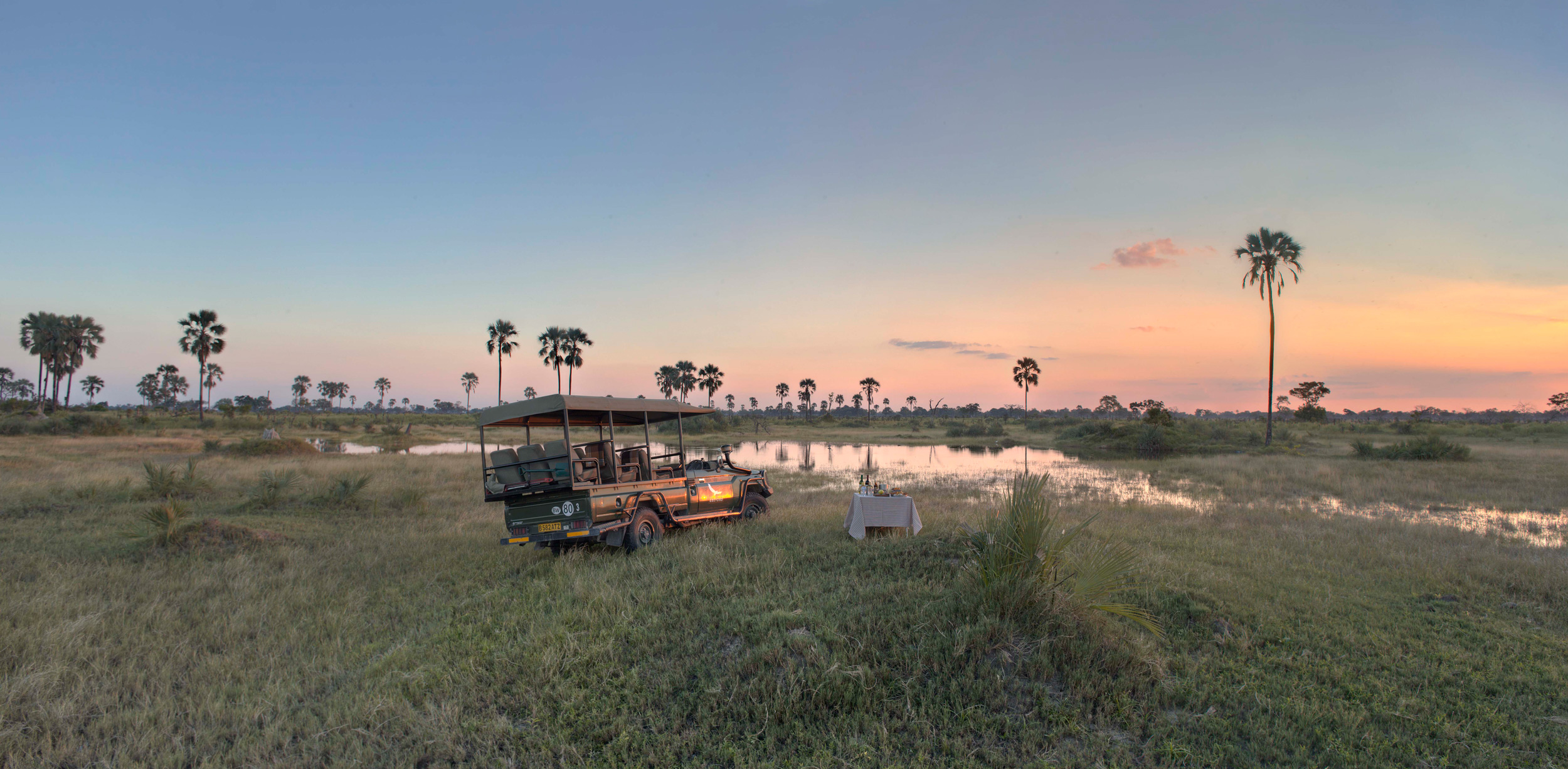 A safari vehicle parked beside flooded grasslands at sunset at Nxabega Okavango Tented Camp in Botswana's Okavango Delta.