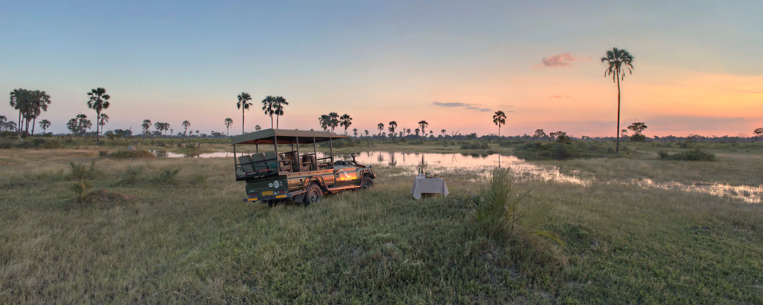 A safari vehicle parked beside flooded grasslands at sunset at Nxabega Okavango Tented Camp in Botswana's Okavango Delta.