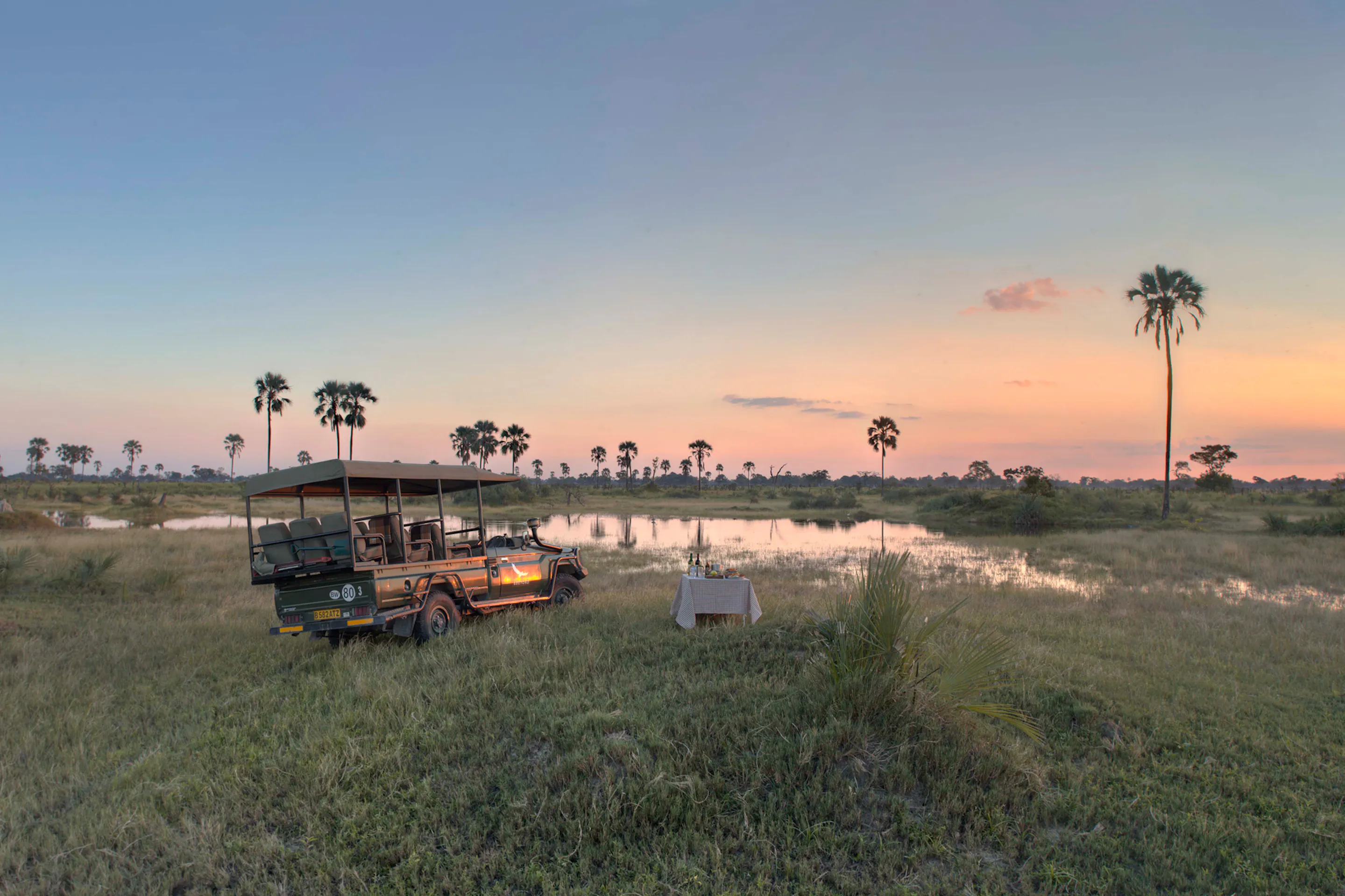A safari vehicle parked beside flooded grasslands at sunset at Nxabega Okavango Tented Camp in Botswana's Okavango Delta.