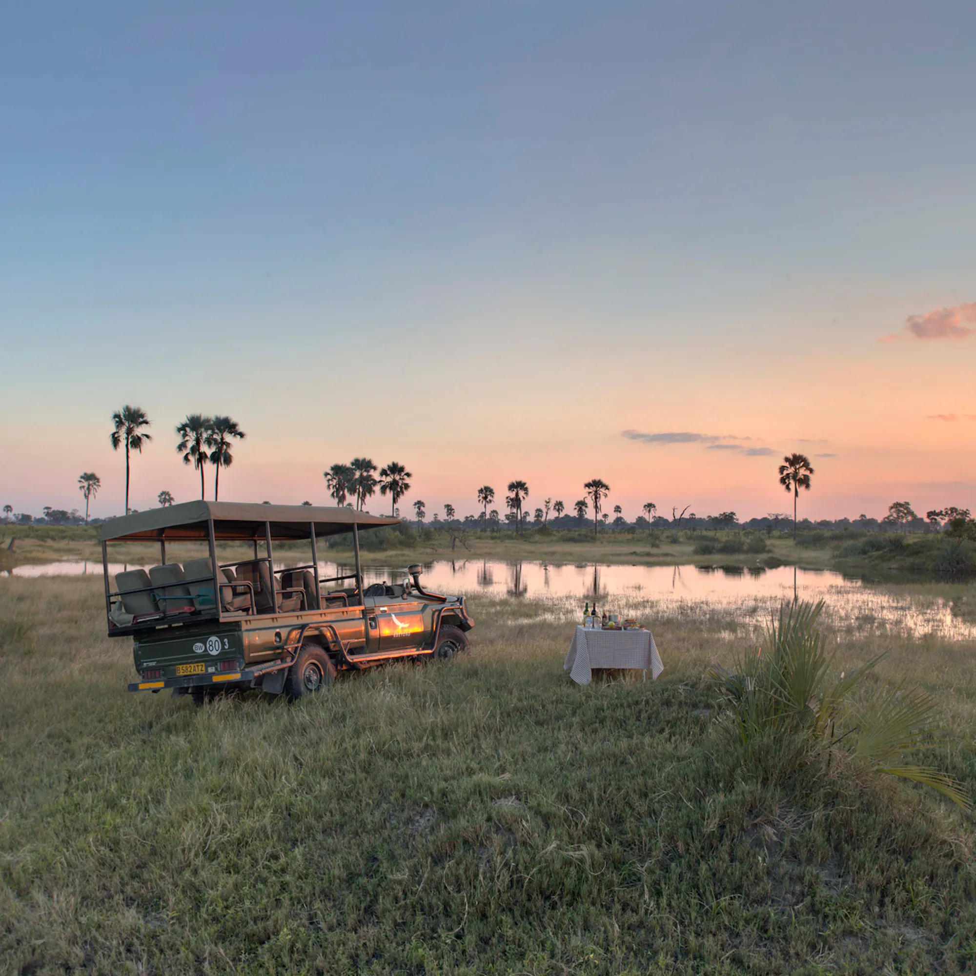 A safari vehicle parked beside flooded grasslands at sunset at Nxabega Okavango Tented Camp in Botswana's Okavango Delta.