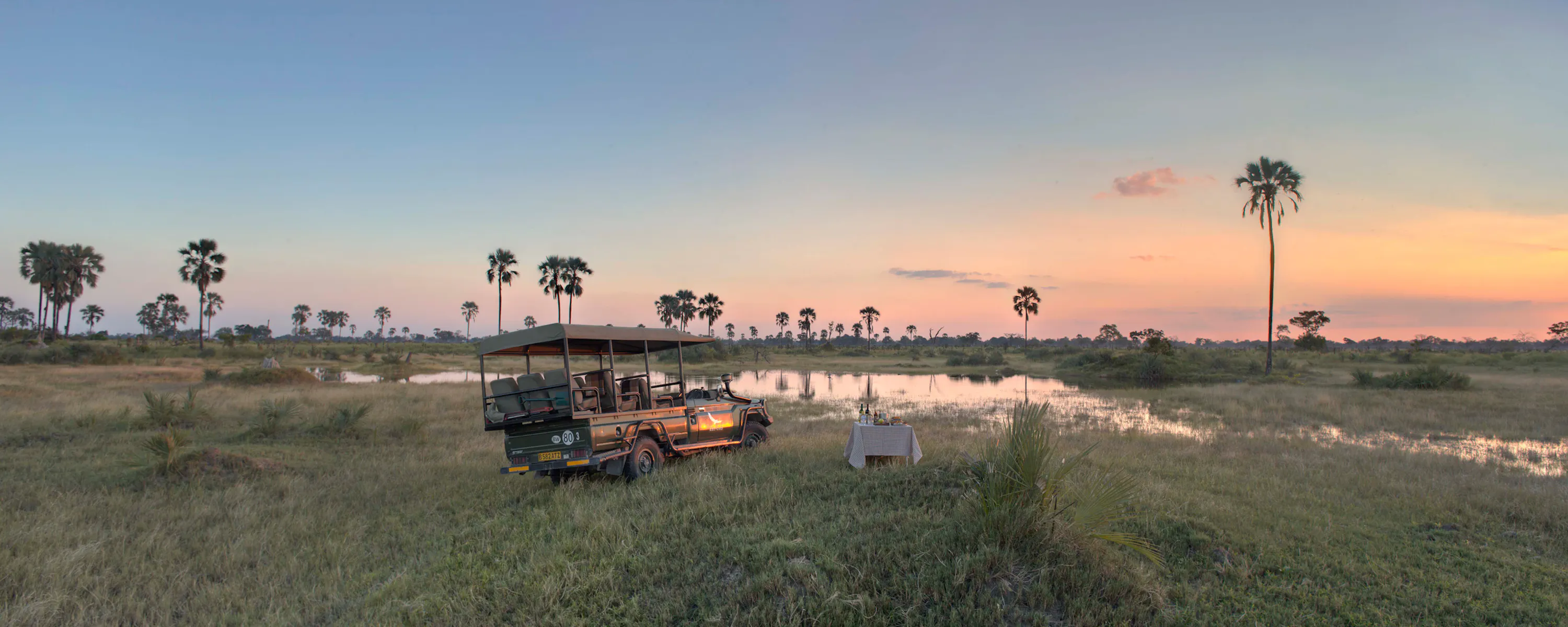 A safari vehicle parked beside flooded grasslands at sunset at Nxabega Okavango Tented Camp in Botswana's Okavango Delta.