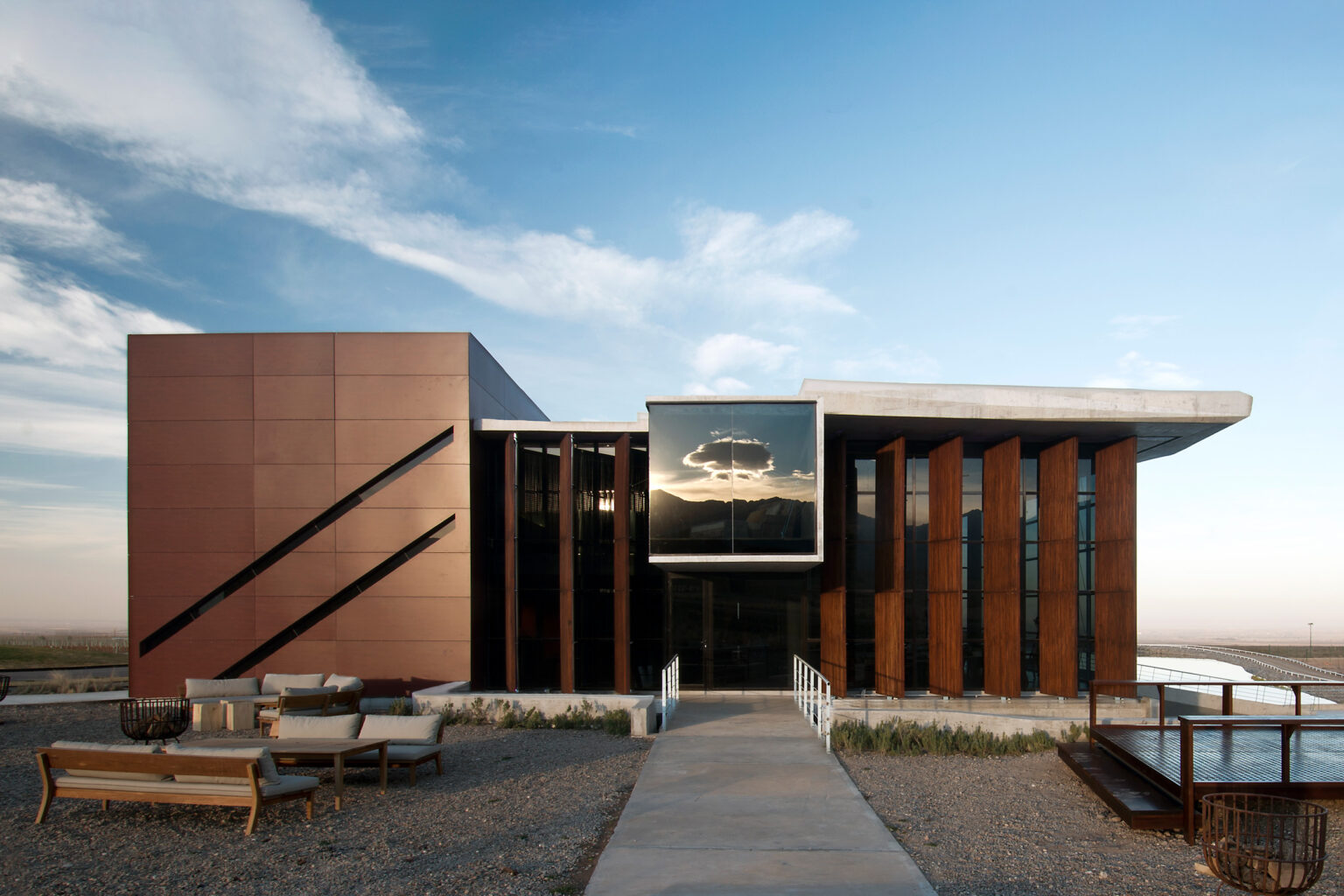 The modern facade of Casa de Uco rises against open sky in Mendoza, Argentina, with grasses and low hills beyond.