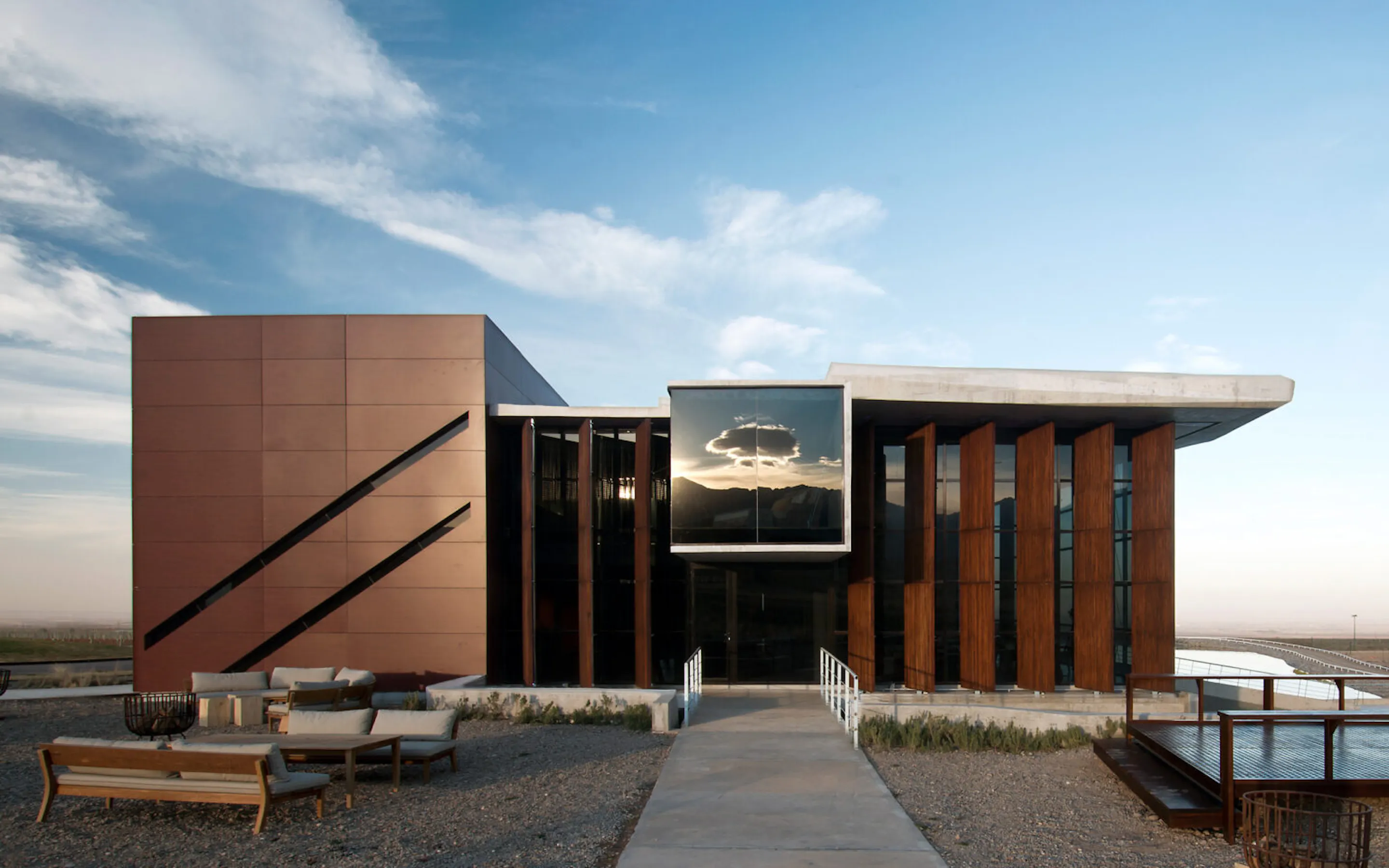 The modern facade of Casa de Uco rises against open sky in Mendoza, Argentina, with grasses and low hills beyond.