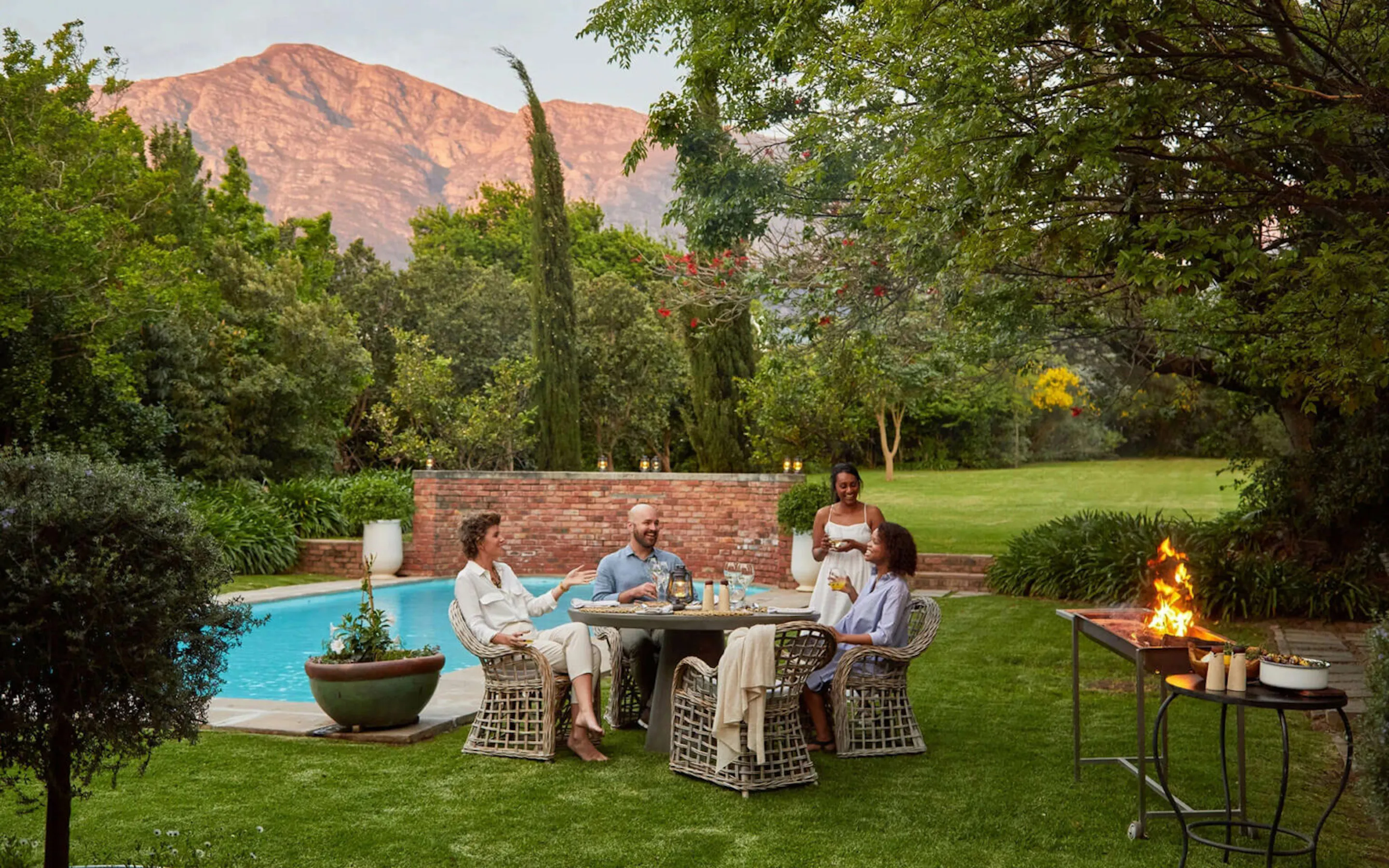Guests gathered around a fire pit in a garden courtyard at La Cle des Montagnes in South Africa's Cape Winelands.
