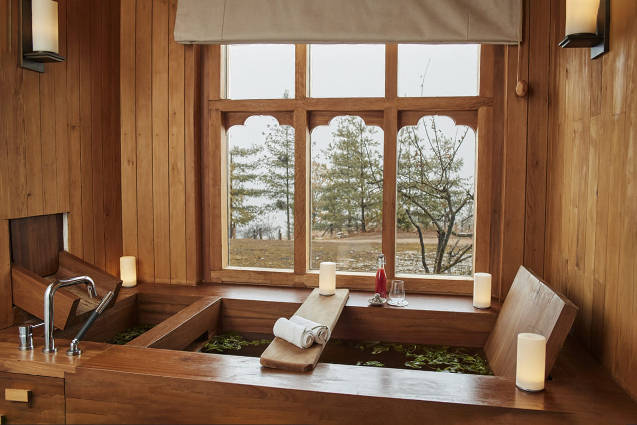 A deep stone soaking tub sits beside a wide window at Six Senses Thimphu, looking over forested Bhutan hills.