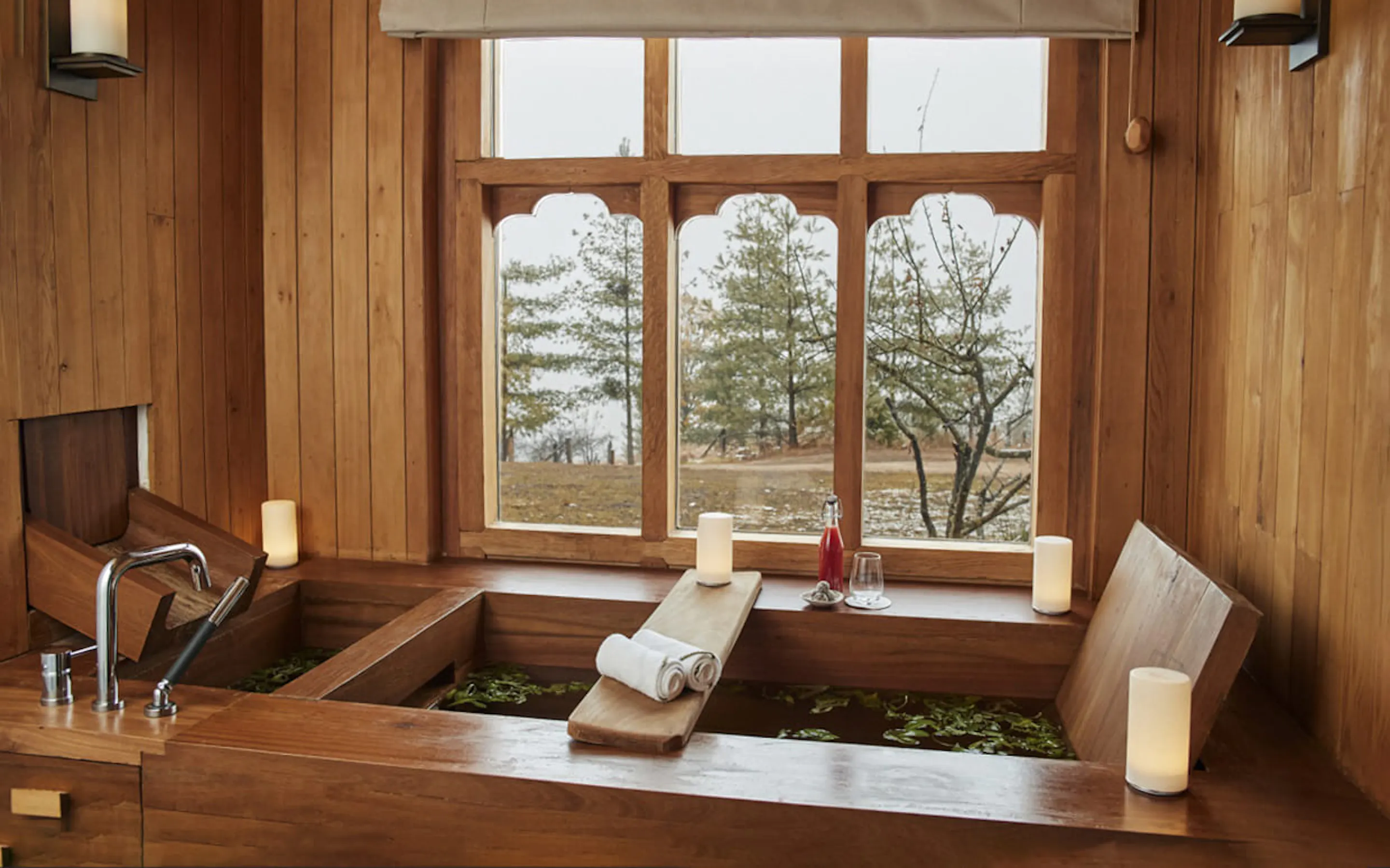 A deep stone soaking tub sits beside a wide window at Six Senses Thimphu, looking over forested Bhutan hills.