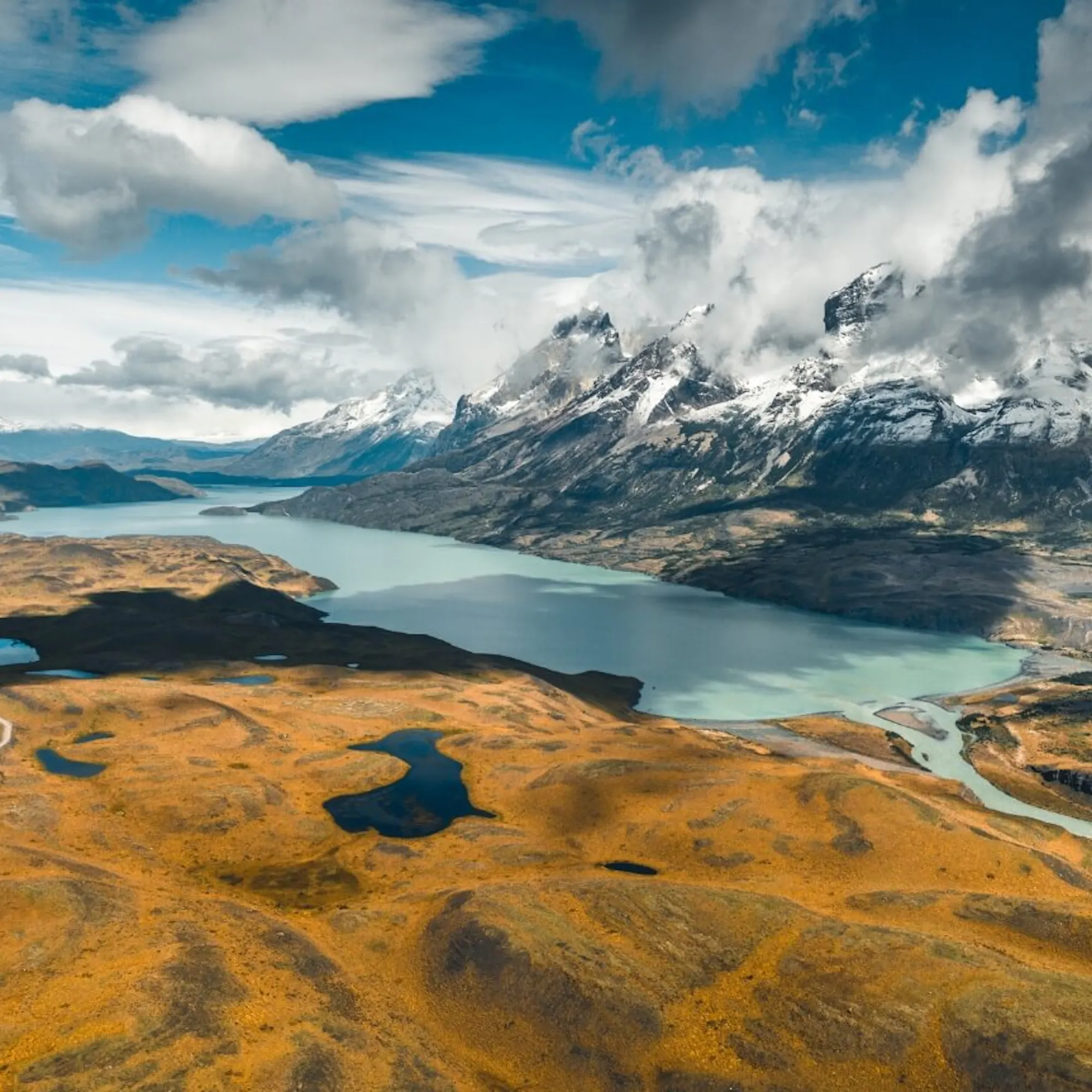 Jagged peaks rise above a Patagonian valley and lake near El Chalten, with rocky slopes cutting into the sky.