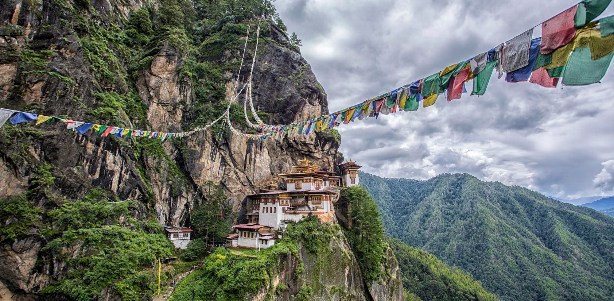 Tiger's Nest Monastery clings to a sheer cliff in Paro, with prayer flags and cloud-filled valleys beyond.