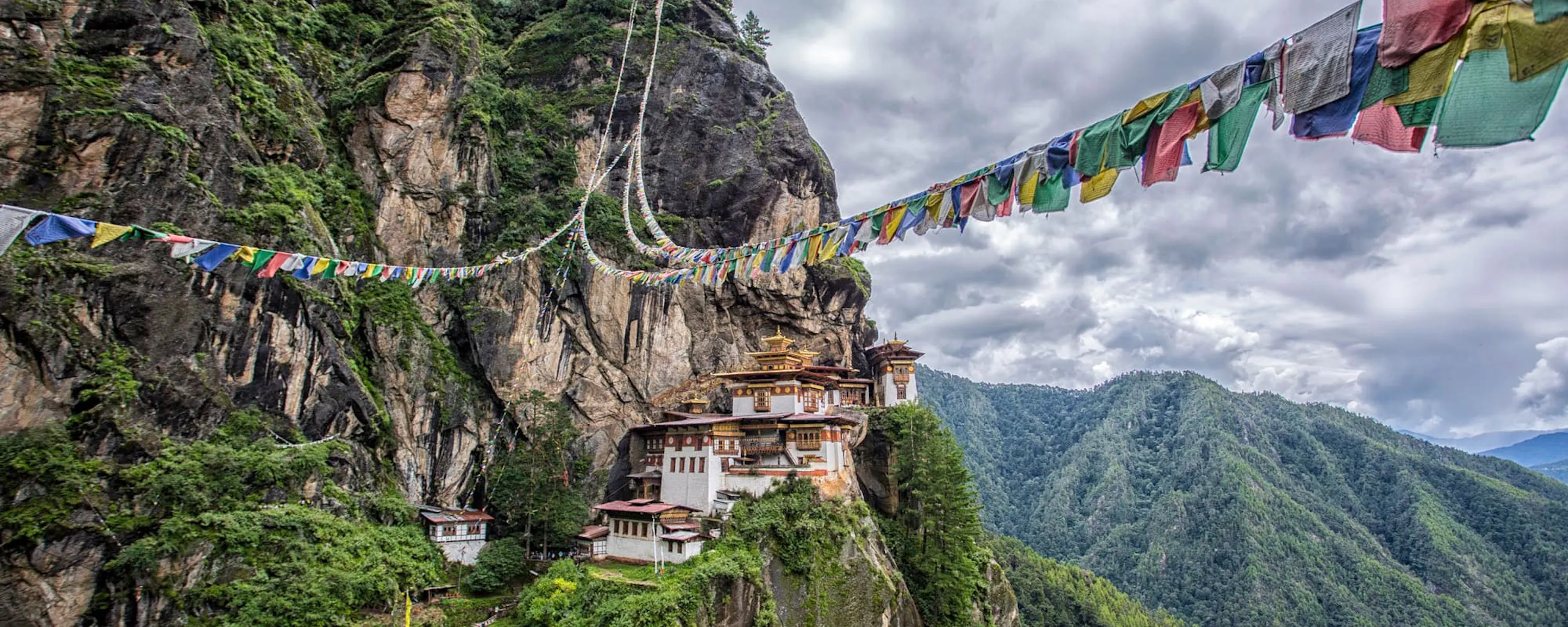 Tiger's Nest Monastery clings to a sheer cliff in Paro, with prayer flags and cloud-filled valleys beyond.