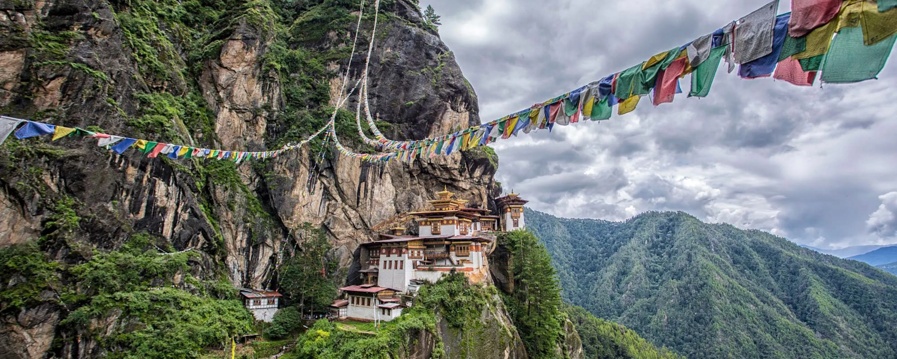 Tiger's Nest Monastery clings to a sheer cliff in Paro, with prayer flags and cloud-filled valleys beyond.