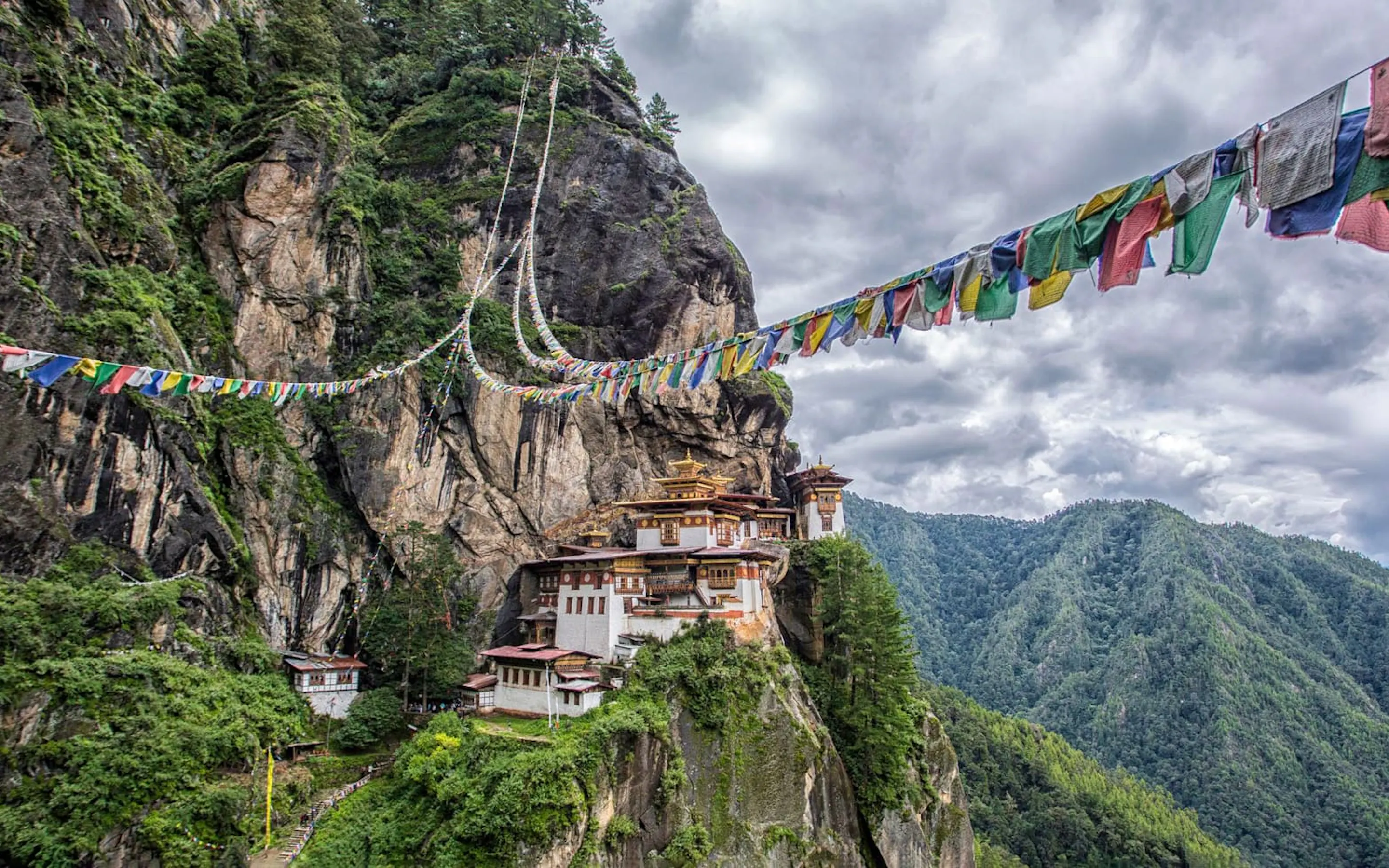 Tiger's Nest Monastery clings to a sheer cliff in Paro, with prayer flags and cloud-filled valleys beyond.