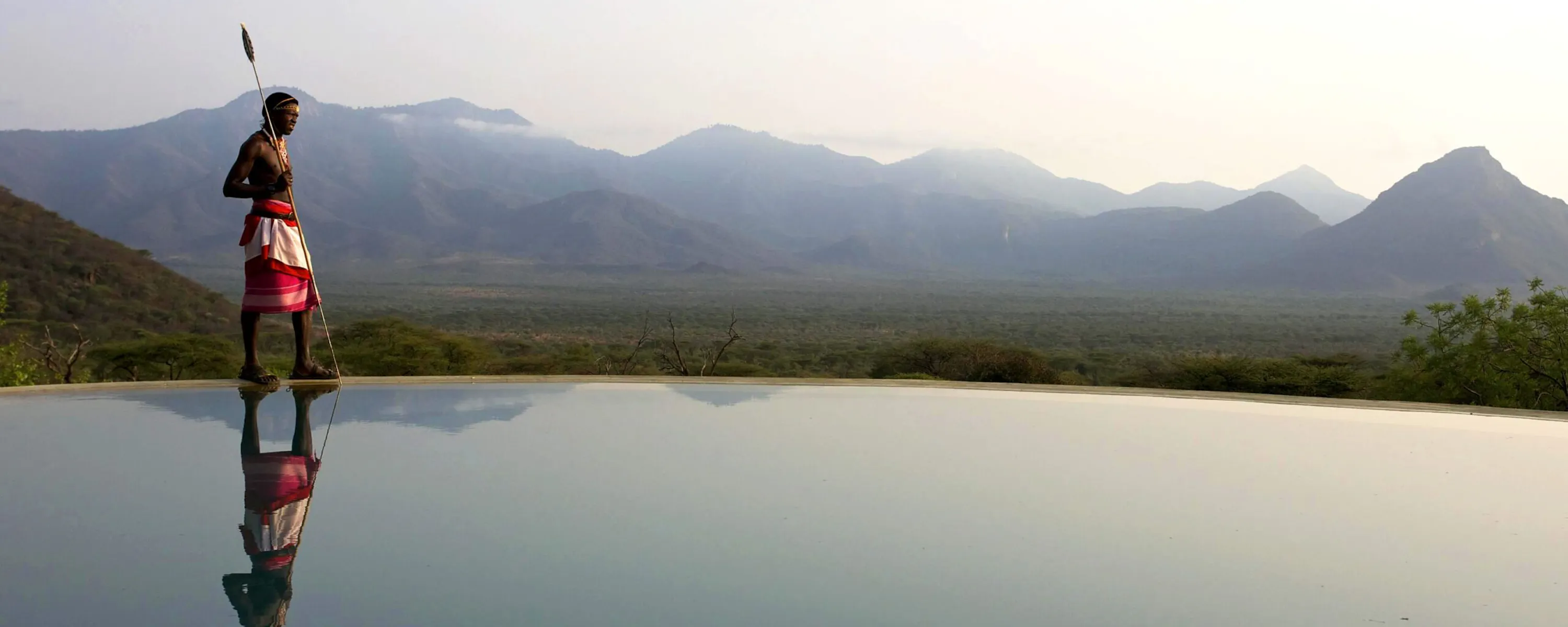 A Maasai man stands beside an infinity pool at Sarara Camp, overlooking the sunlit hills of northern Kenya.
