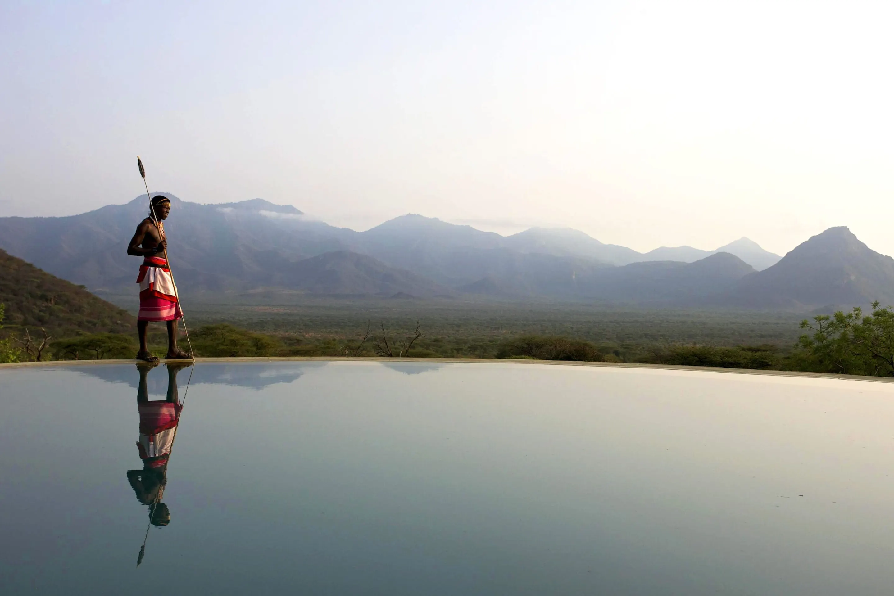 A Maasai man stands beside an infinity pool at Sarara Camp, overlooking the sunlit hills of northern Kenya.