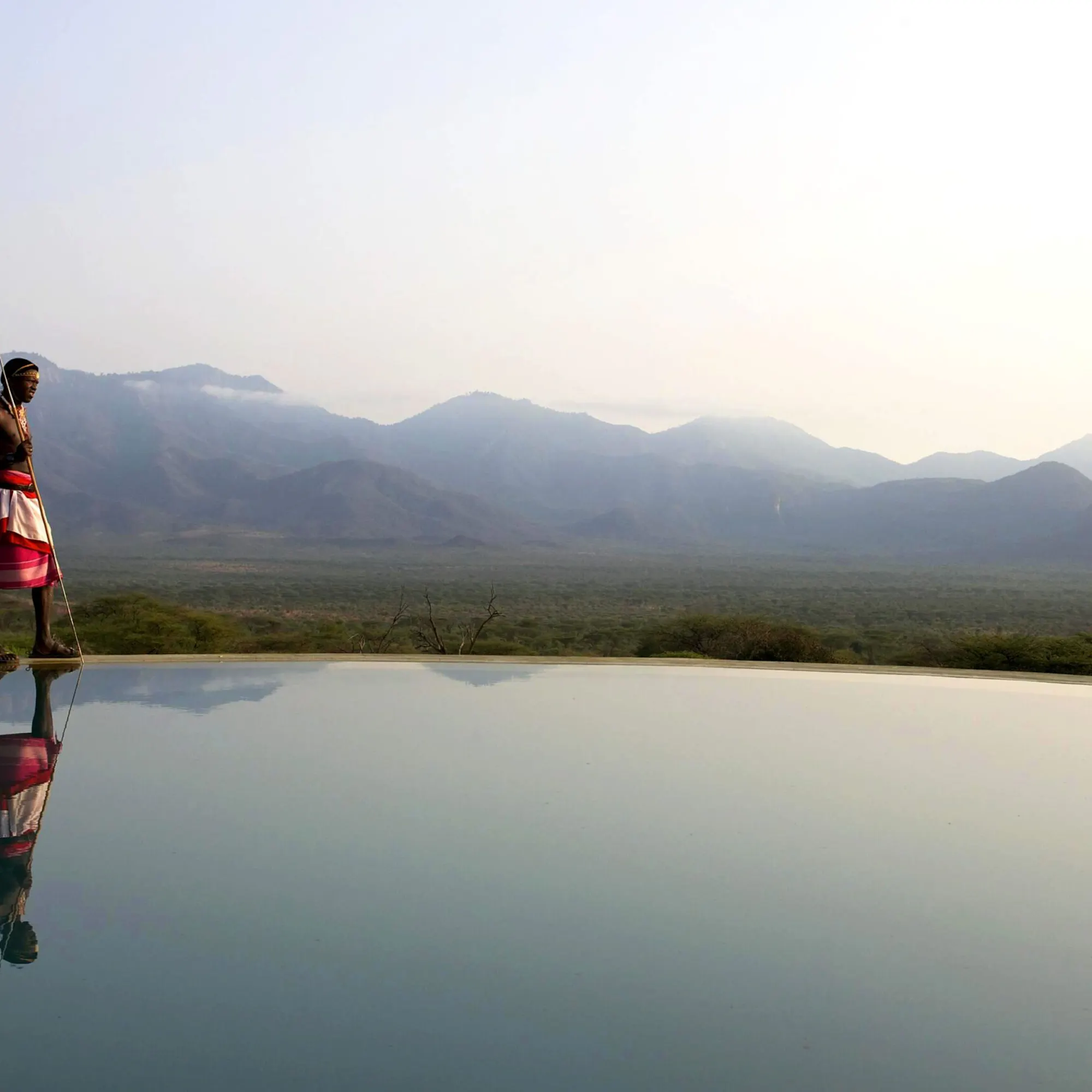 A Maasai man stands beside an infinity pool at Sarara Camp, overlooking the sunlit hills of northern Kenya.