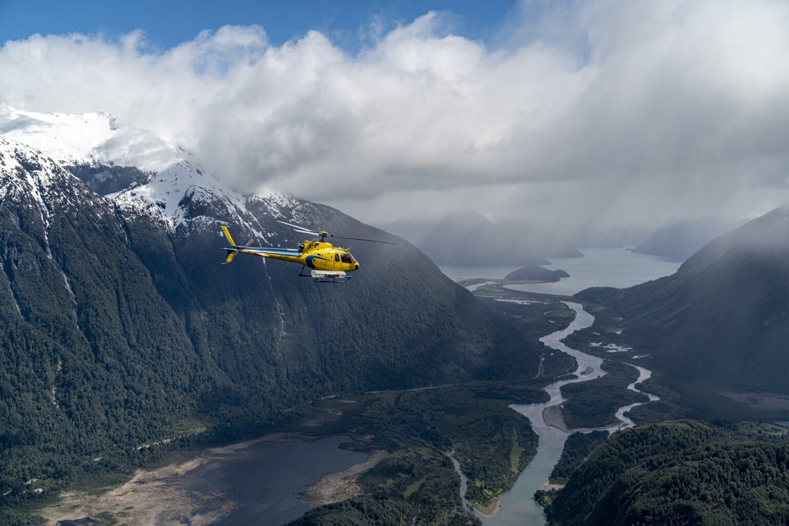 A yellow helicopter flies above deep green valleys and braided rivers near Rio Palena Lodge in Chilean Patagonia.