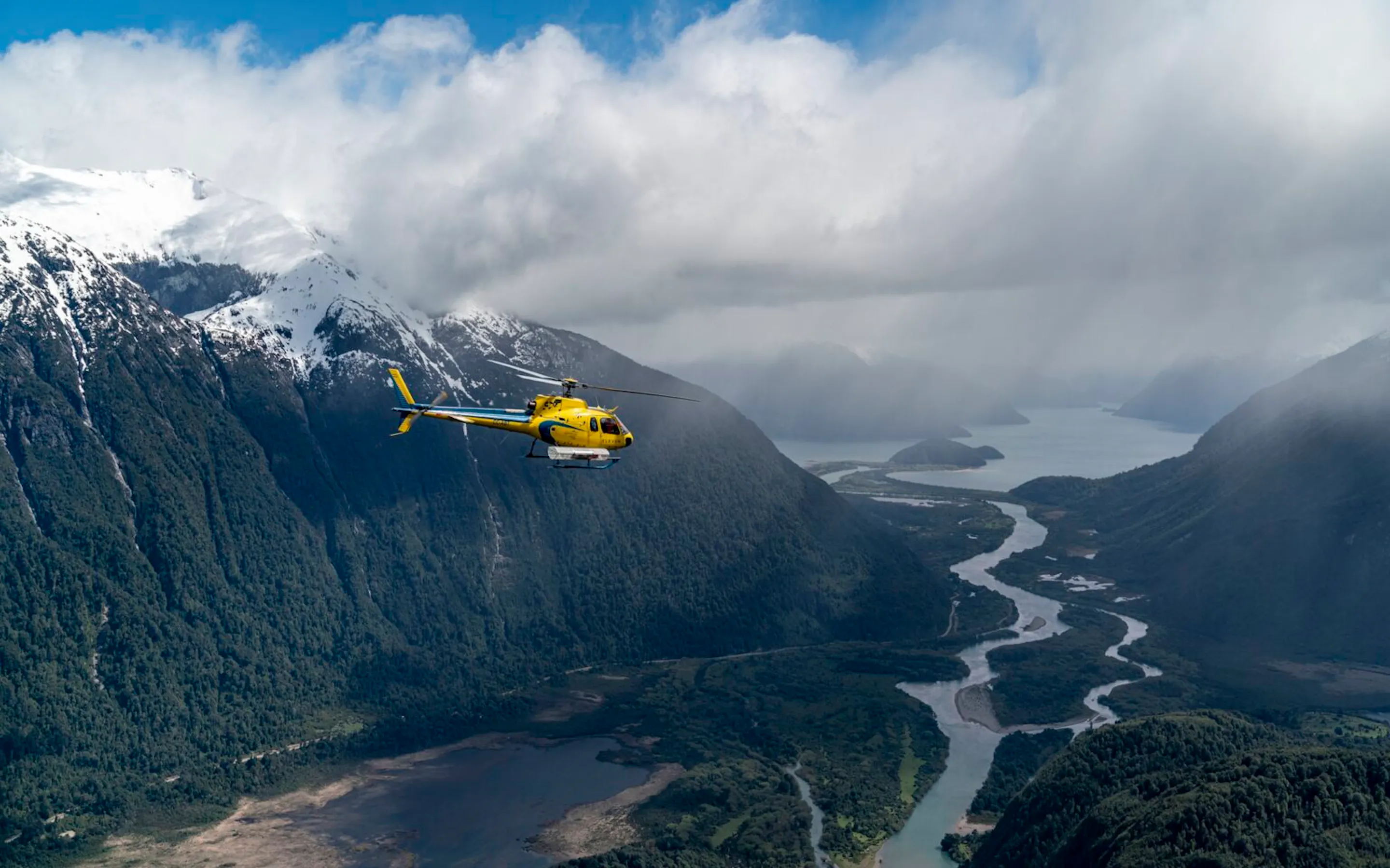 A yellow helicopter flies above deep green valleys and braided rivers near Rio Palena Lodge in Chilean Patagonia.