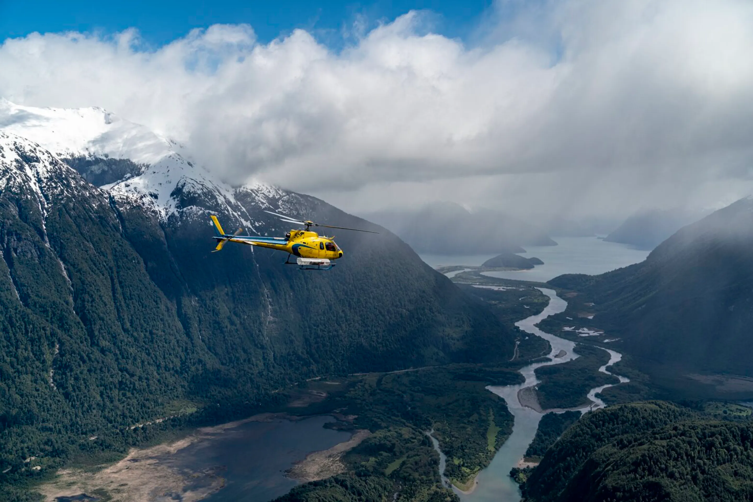 A yellow helicopter flies above deep green valleys and braided rivers near Rio Palena Lodge in Chilean Patagonia.