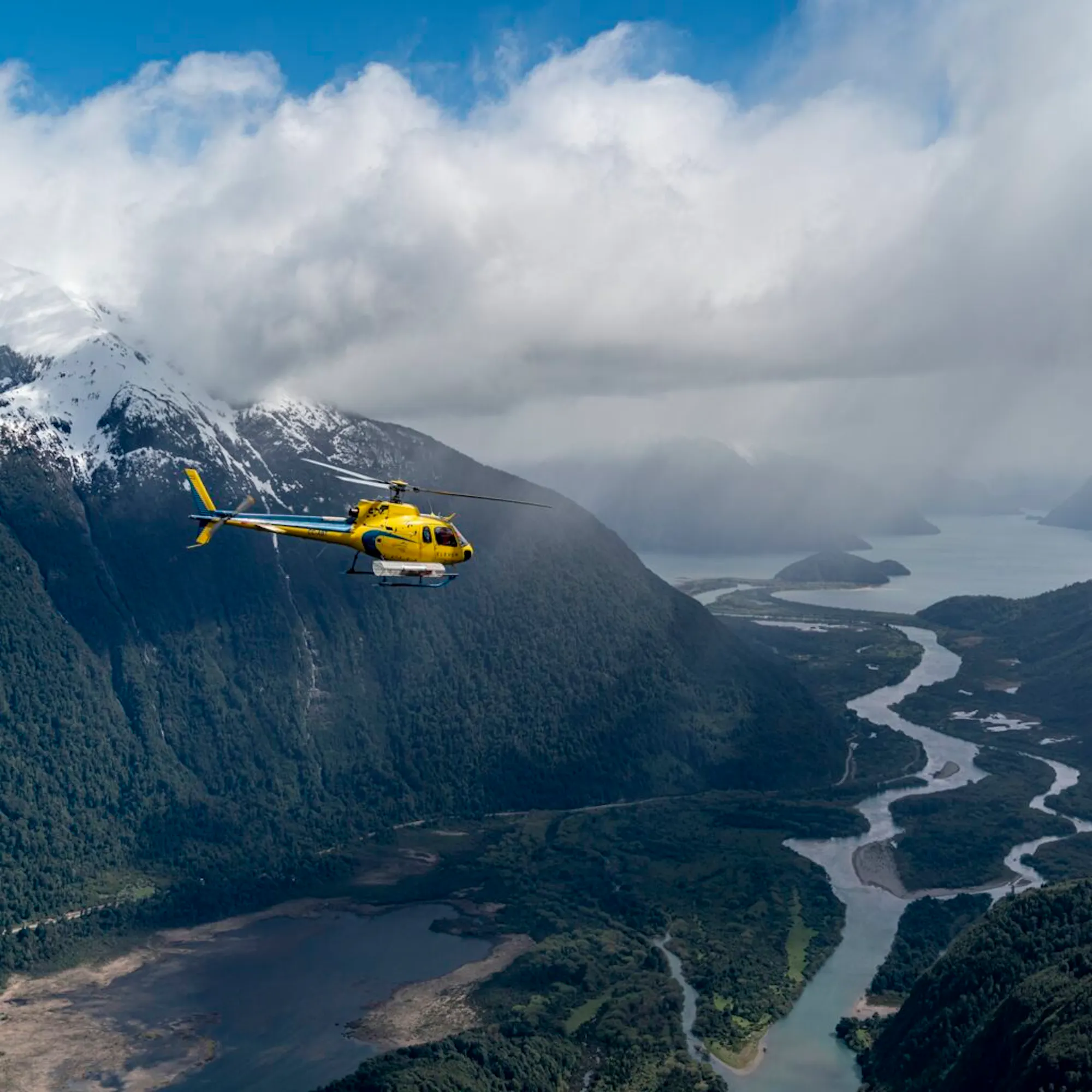 A yellow helicopter flies above deep green valleys and braided rivers near Rio Palena Lodge in Chilean Patagonia.