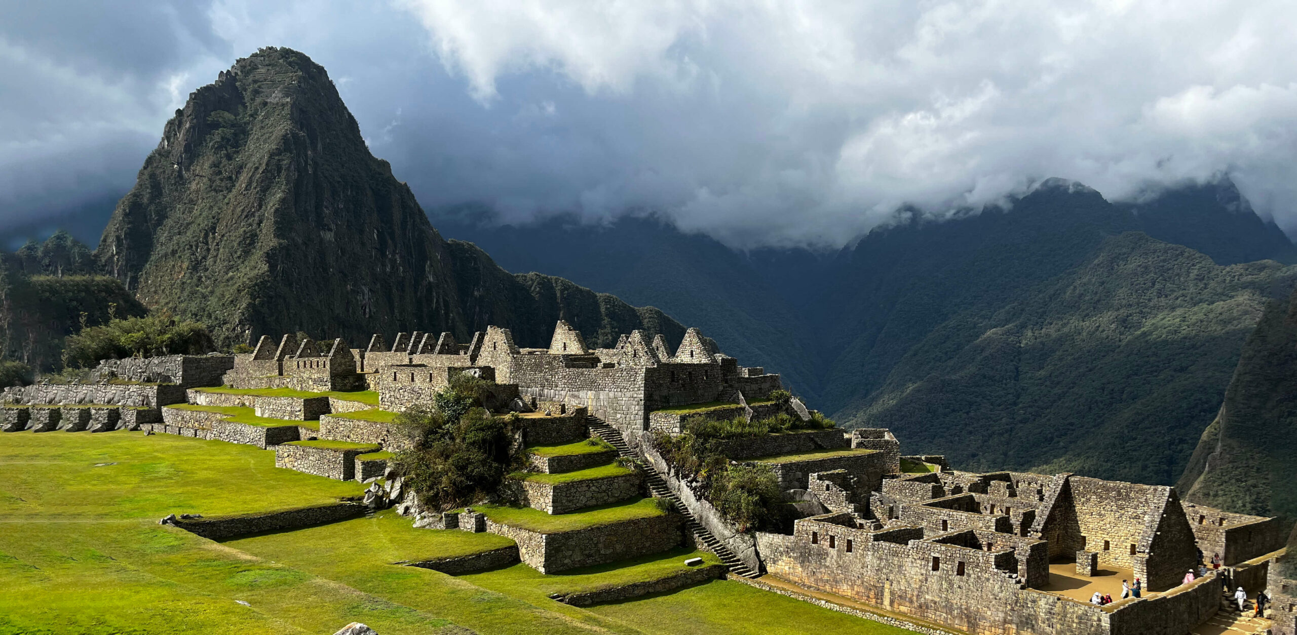 Machu Picchu's stone terraces and temples unfold below steep green peaks beneath thick morning cloud in Peru.