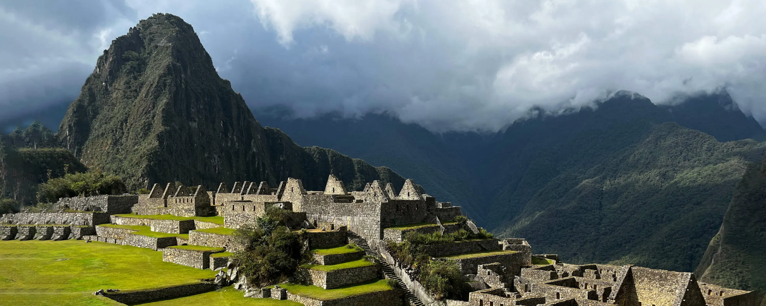 Machu Picchu's stone terraces and temples unfold below steep green peaks beneath thick morning cloud in Peru.