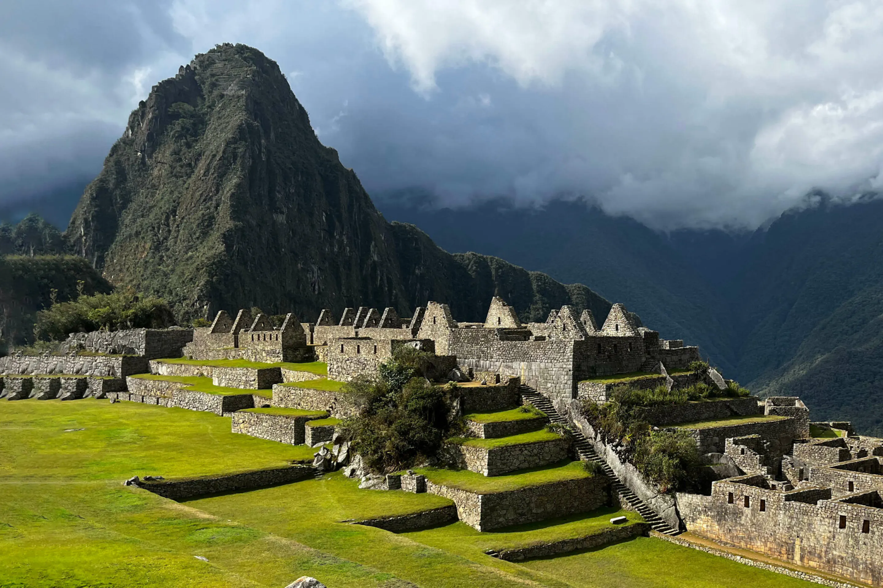 Machu Picchu's stone terraces and temples unfold below steep green peaks beneath thick morning cloud in Peru.