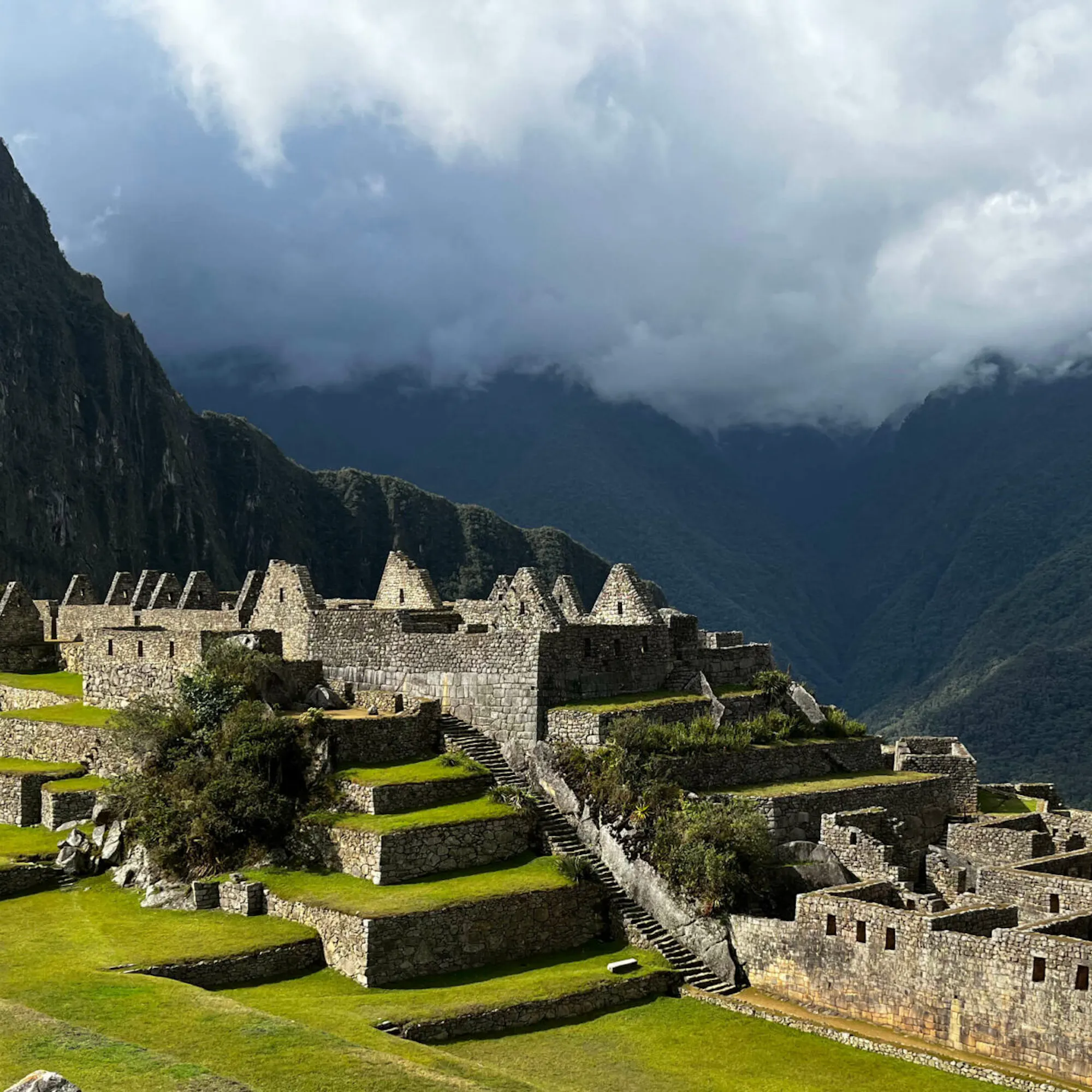 Machu Picchu's stone terraces and temples unfold below steep green peaks beneath thick morning cloud in Peru.