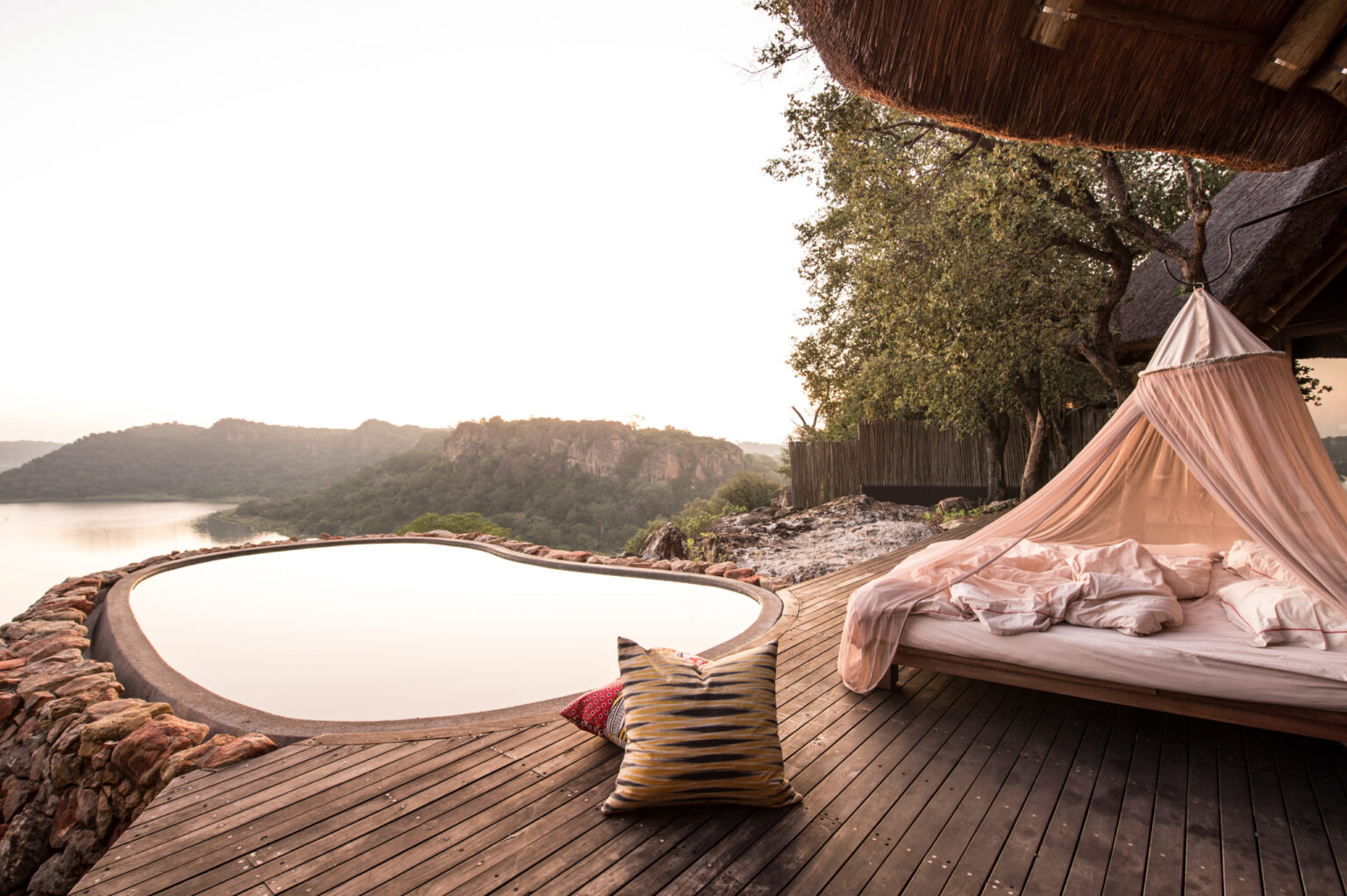 A star bed overlooking still water and distant hills at dusk at Singita Pamushana in Zimbabwe's Malilangwe Reserve.