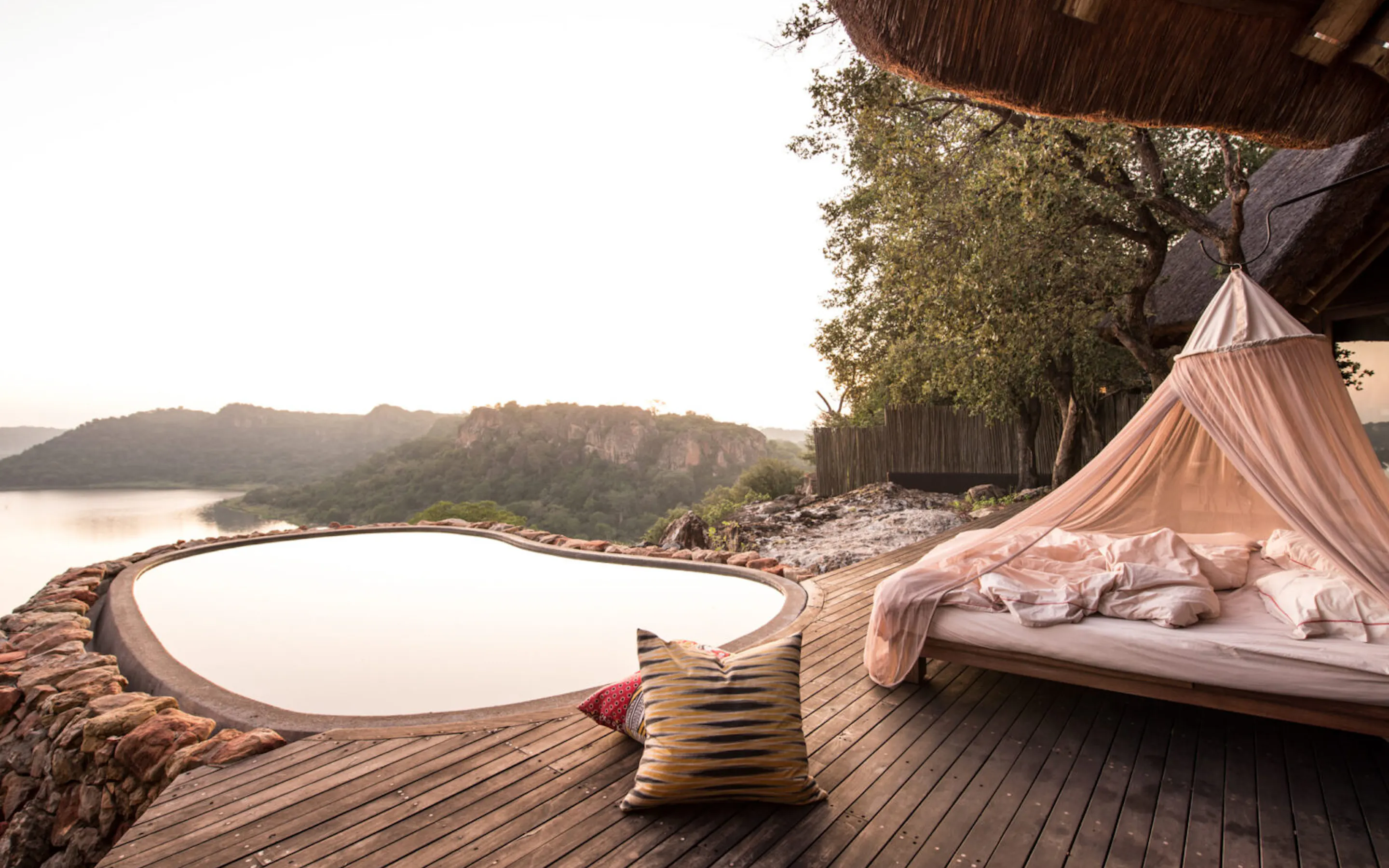 A star bed overlooking still water and distant hills at dusk at Singita Pamushana in Zimbabwe's Malilangwe Reserve.