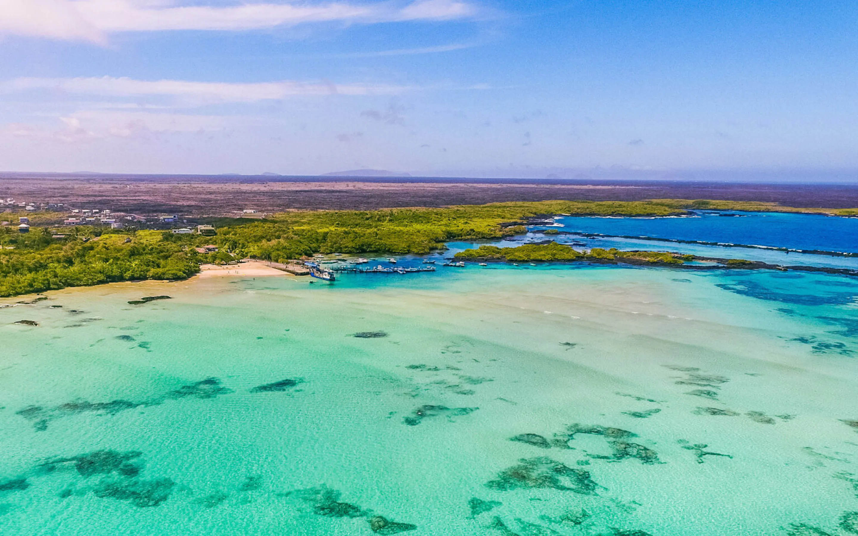 An aerial view shows Isabela Island coastline in the Galapagos, with bright blue sea and dark volcanic shore.