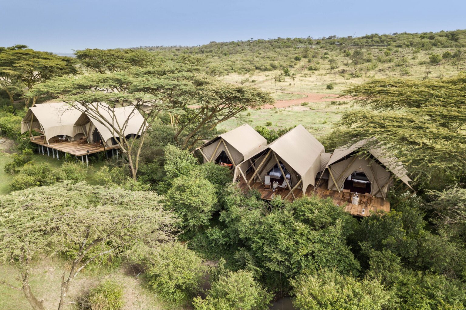 Canvas tents cluster above the Maasai Mara at Mara Nyika, surrounded by rolling green hills and open plains.