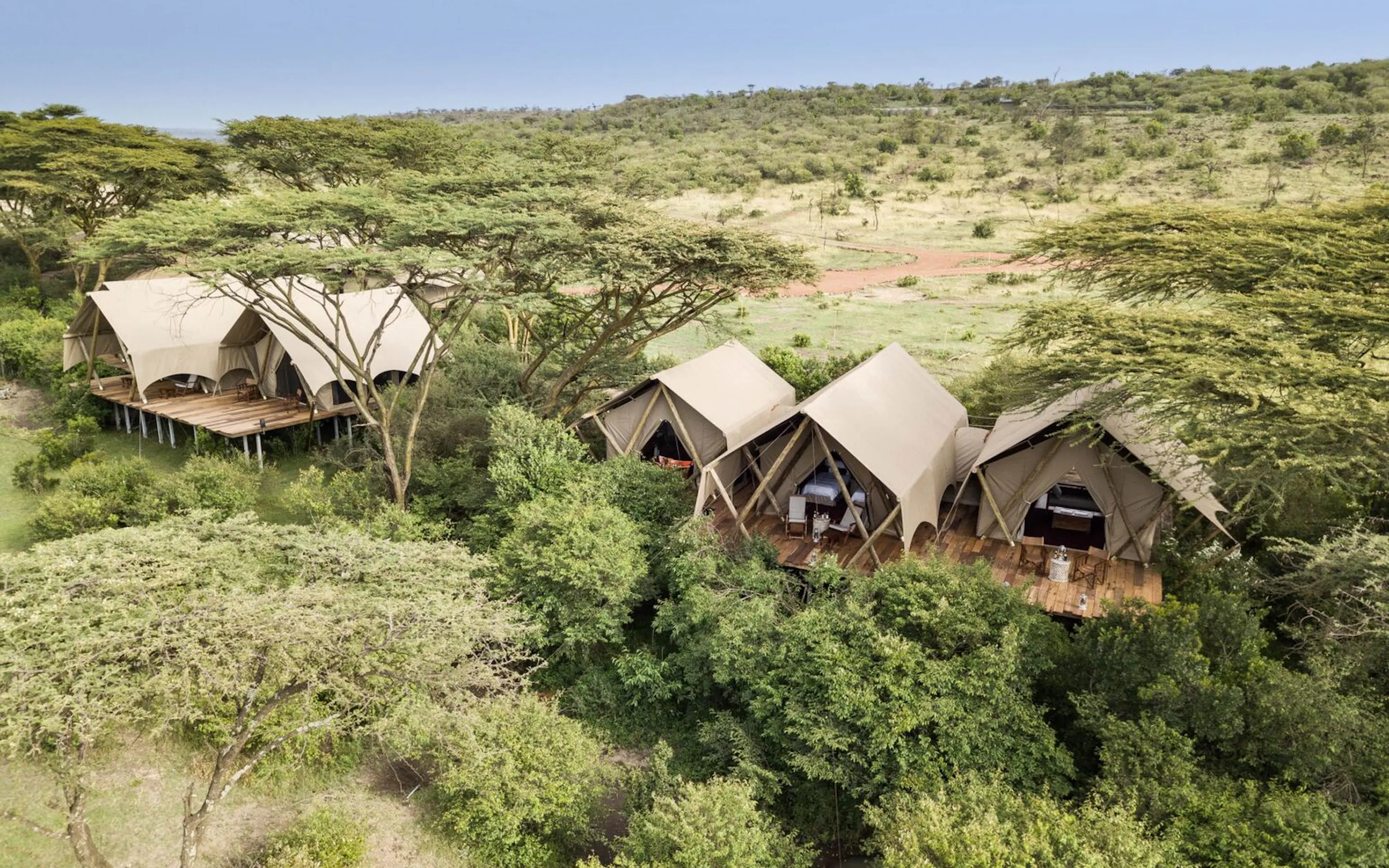 Canvas tents cluster above the Maasai Mara at Mara Nyika, surrounded by rolling green hills and open plains.