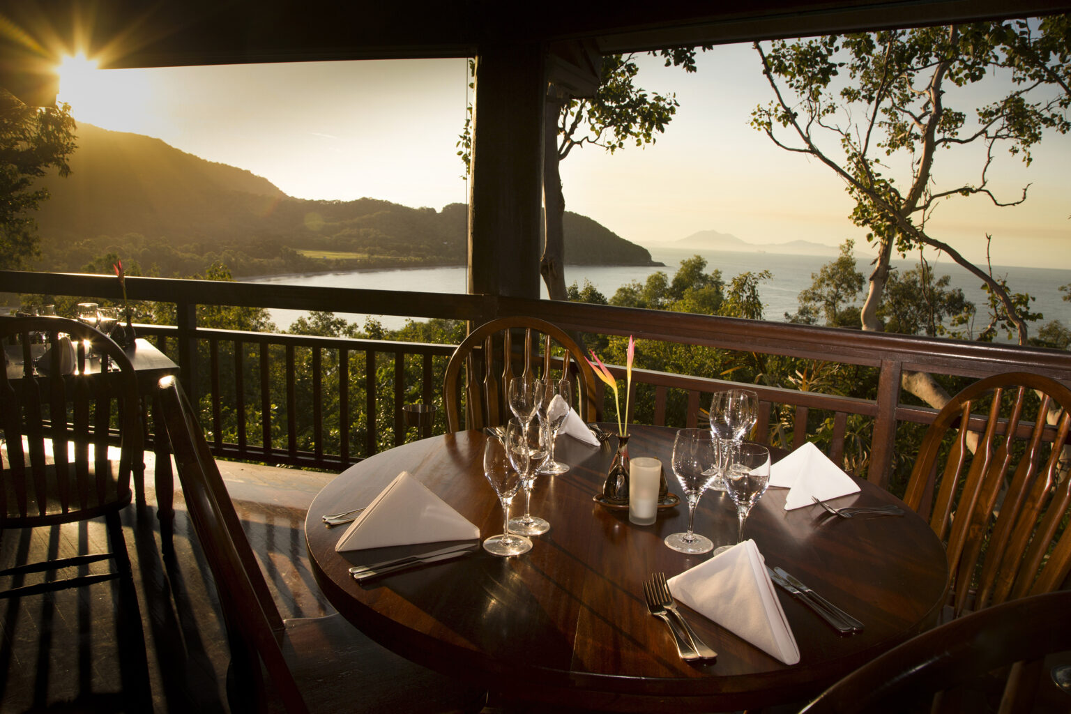 A set table waits on a wooden terrace at Thala Beach Lodge, facing sunrise over Oak Beach and the Coral Sea.