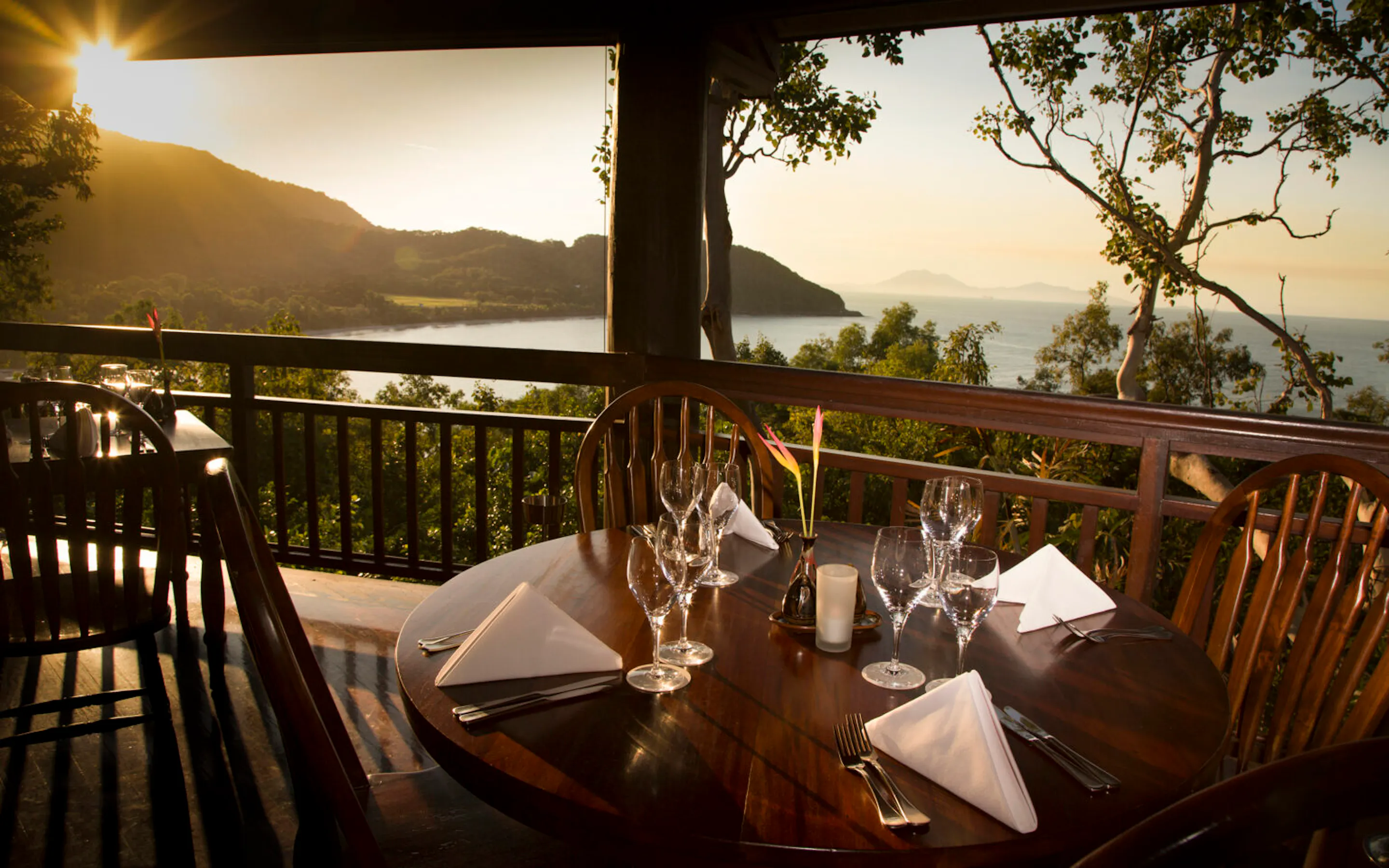 A set table waits on a wooden terrace at Thala Beach Lodge, facing sunrise over Oak Beach and the Coral Sea.