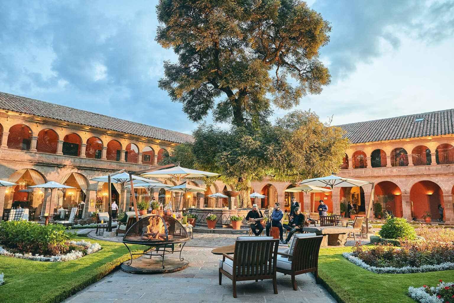 A colonial courtyard at Belmond Monasterio fills with musicians, cafe tables, and a tall tree in the heart of Cusco.