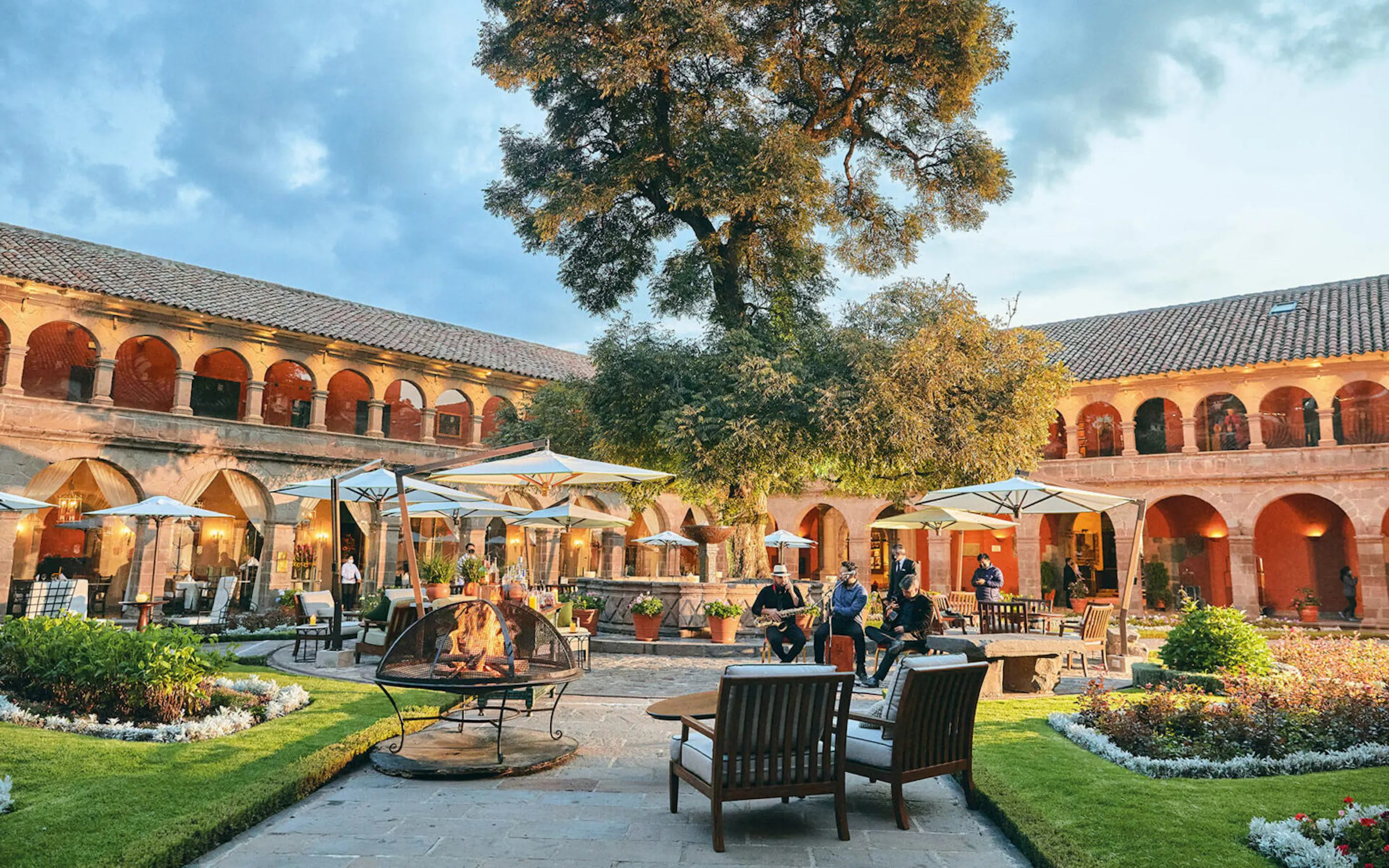A colonial courtyard at Belmond Monasterio fills with musicians, cafe tables, and a tall tree in the heart of Cusco.