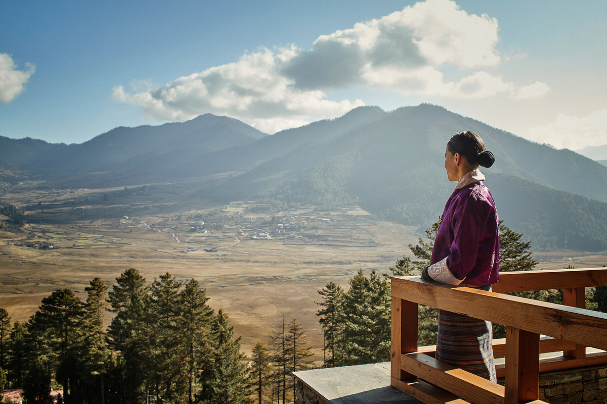 A host looks out over the wide Phobjikha Valley from Six Senses Gangtey, framed by terrace and mountains.